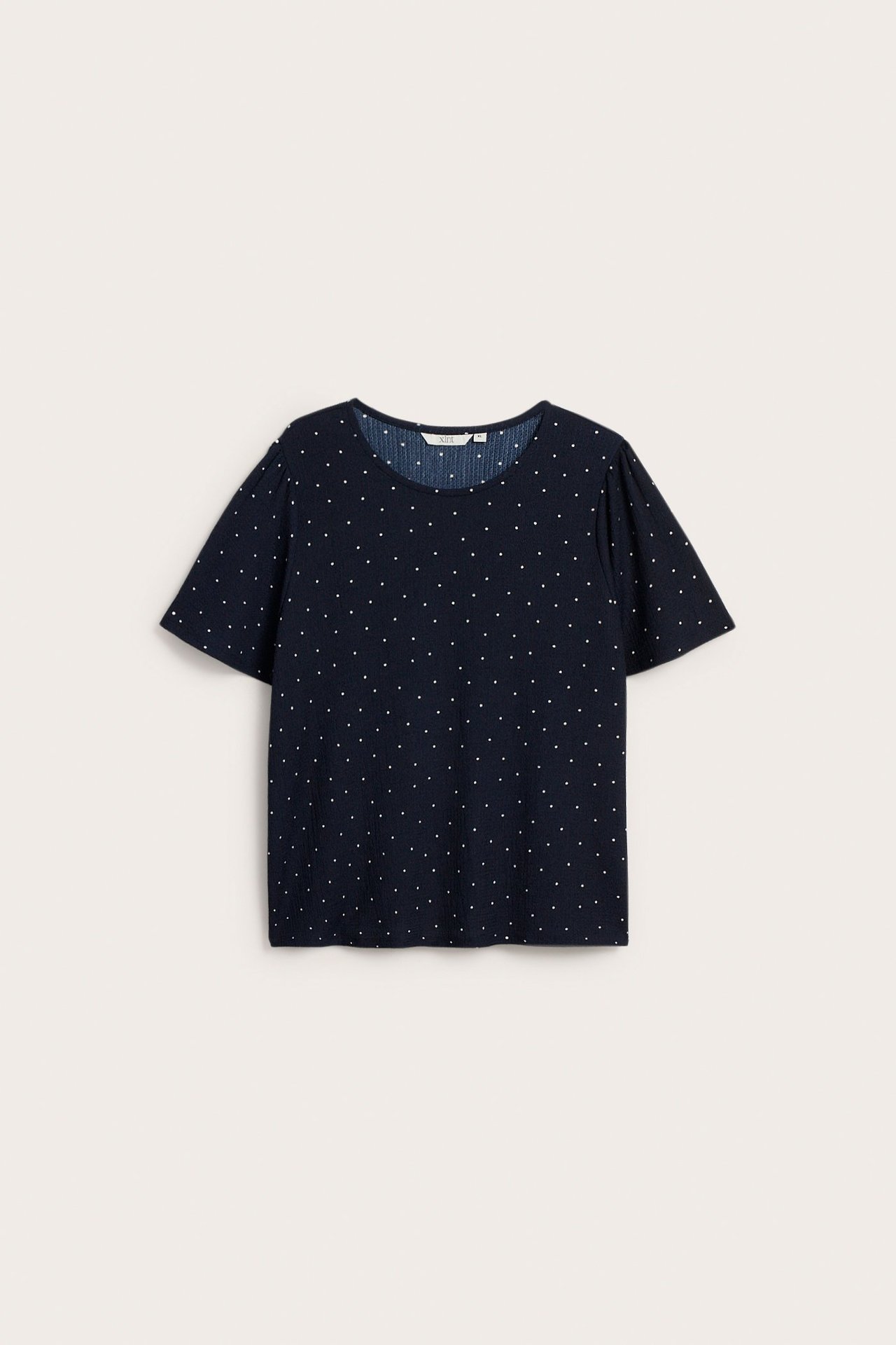 Frontvisning av en mørkeblå kortarmet polyestertopp med hvite prikker og rund hals.