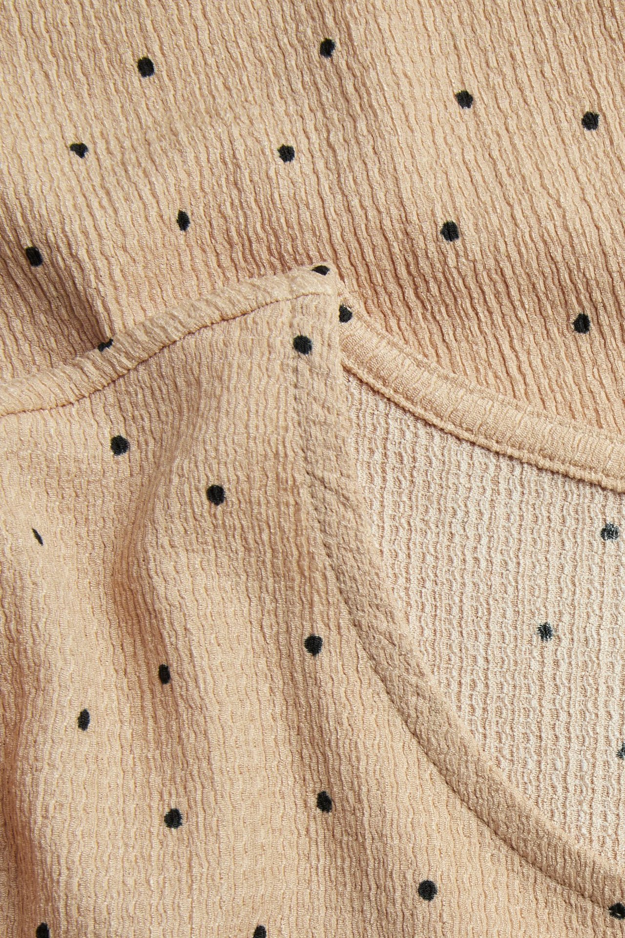 Nærbilde av en beige strukturert prikkete topp med små svarte prikker.