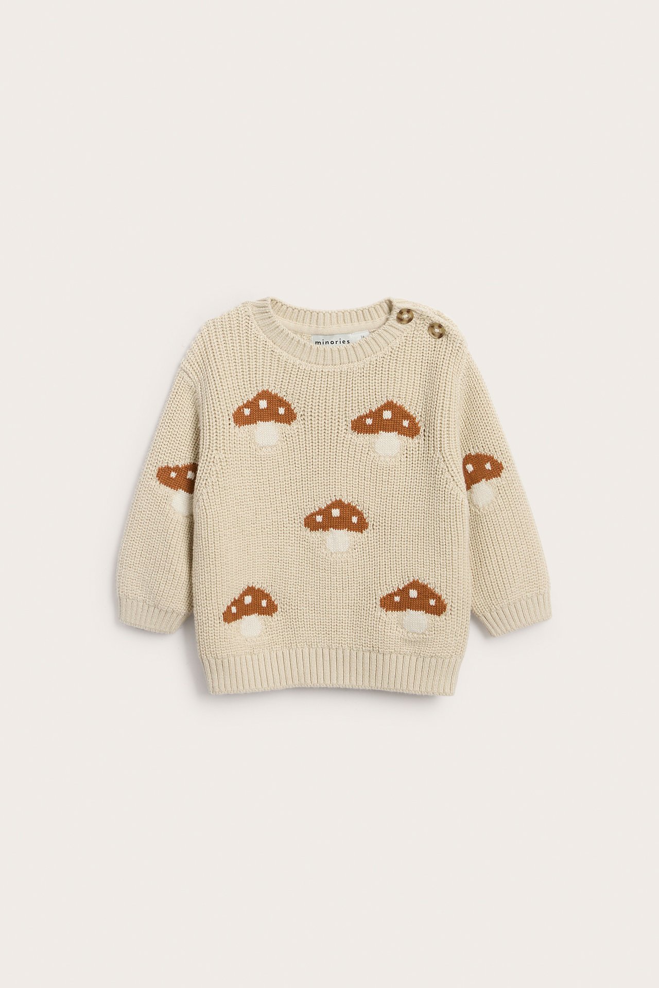 Frontbilde av en beige strikkegenser for baby med brune soppmønstre og to skulderknapper.