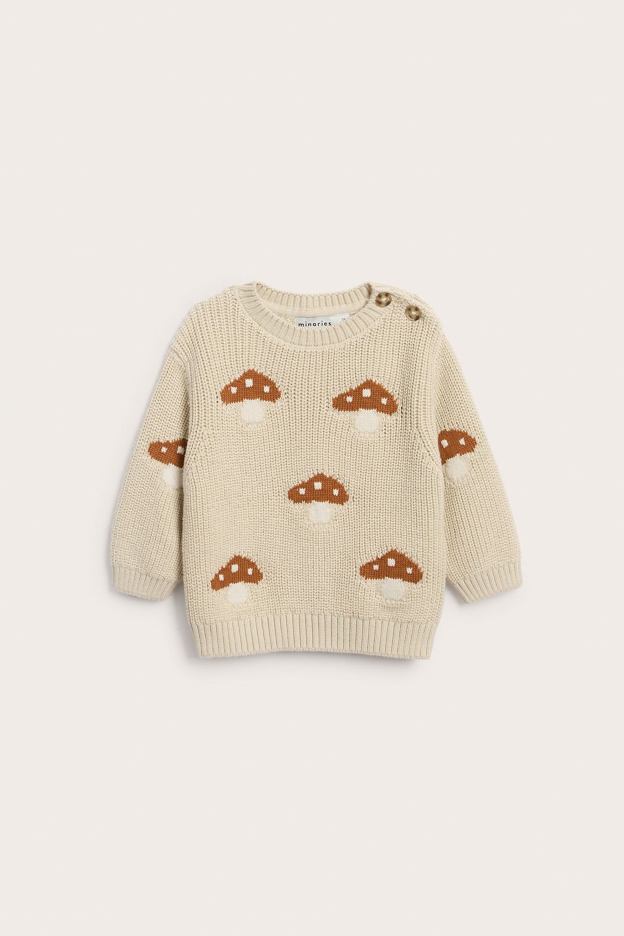 Frontbilde av en beige strikkegenser for baby med brune soppmønstre og to skulderknapper.