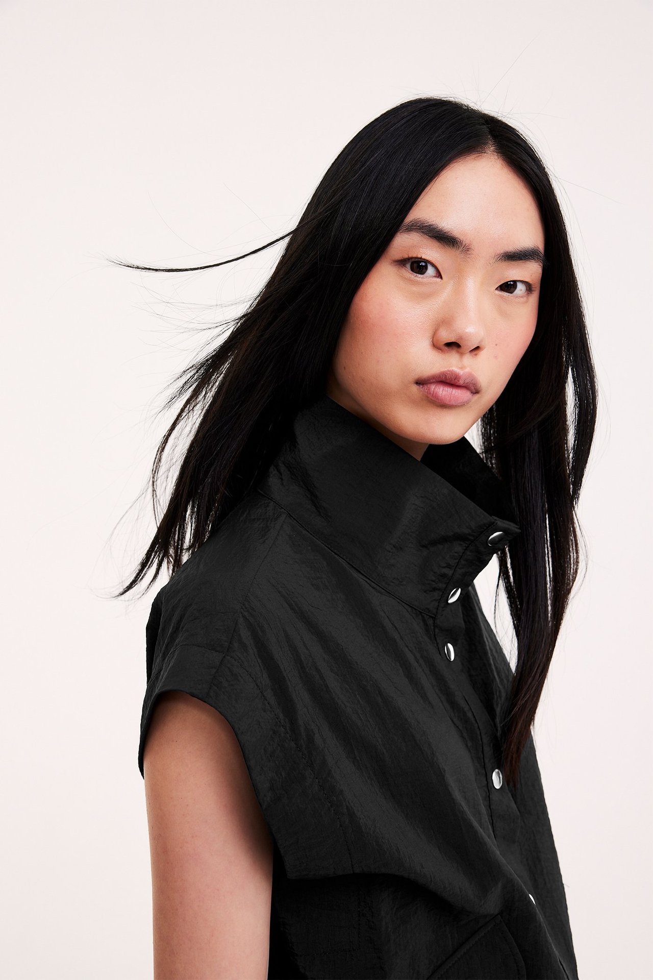 Zbliżenie, widok z boku: kobieta w czarnej, bezrękawnikowej koszuli z poliamidu, z wysokim kołnierzem, srebrnymi zatrzaskami.