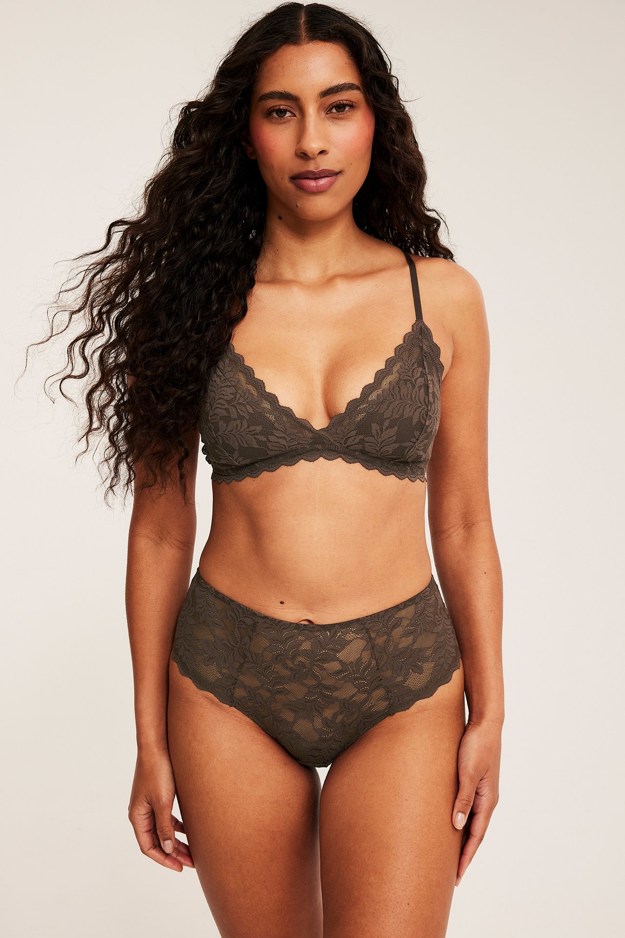 Framifrån: kvinnlig modell i mörk olivgrön spets-bralette och matchande högmidjade trosor.