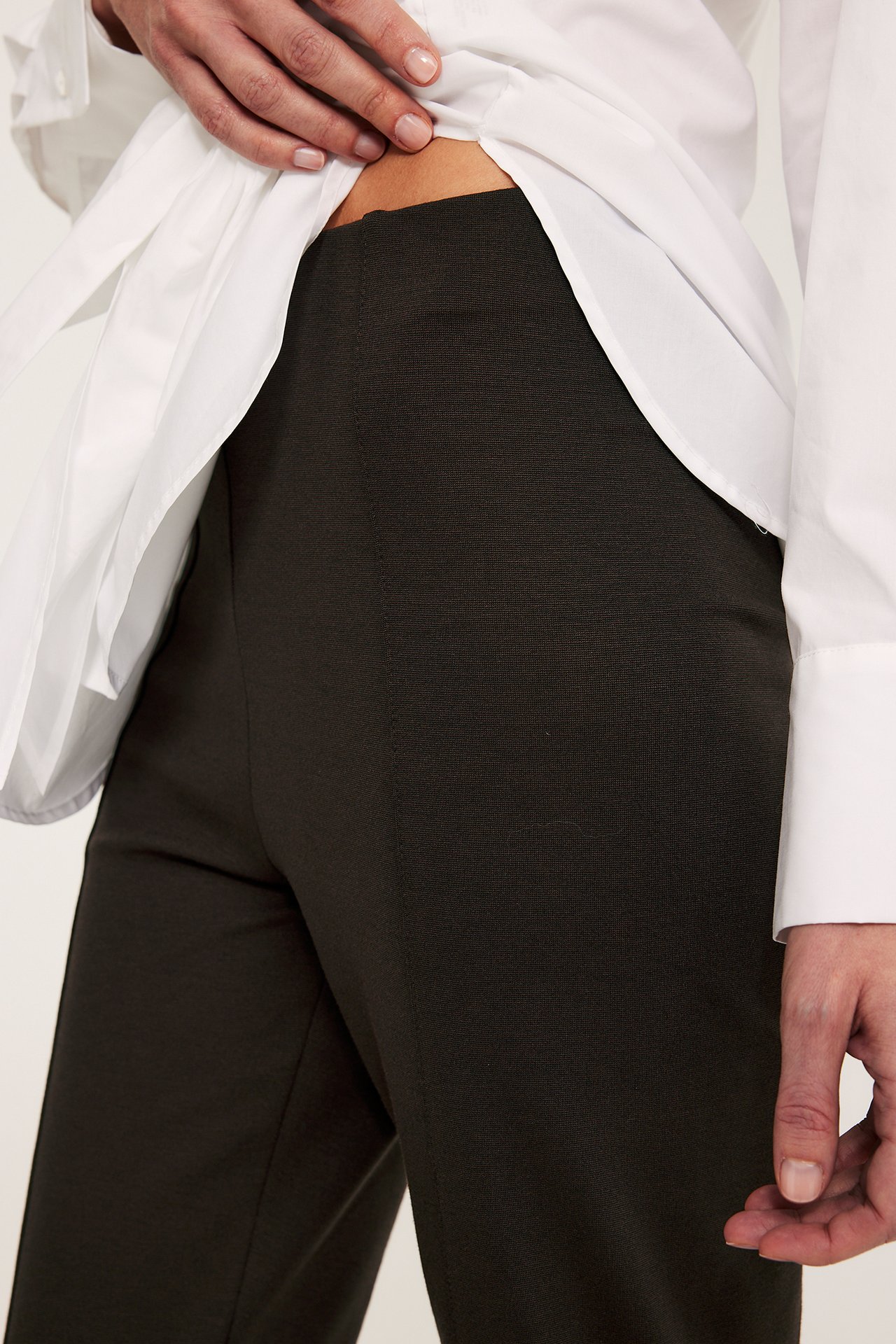 Zbliżenie kobiety w ciemnobrązowych prostych spodniach pull-on z przednim szwem i białej koszuli.