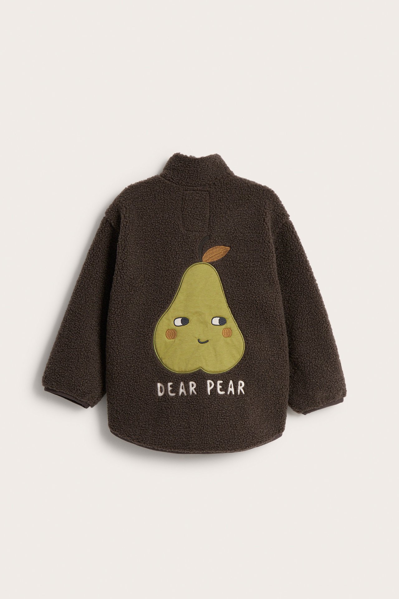 Ryggvisning av en barns mørkebrun teddyfleecejakke med grønn pæreansiktapplikasjon og 'DEAR PEAR' tekst.
