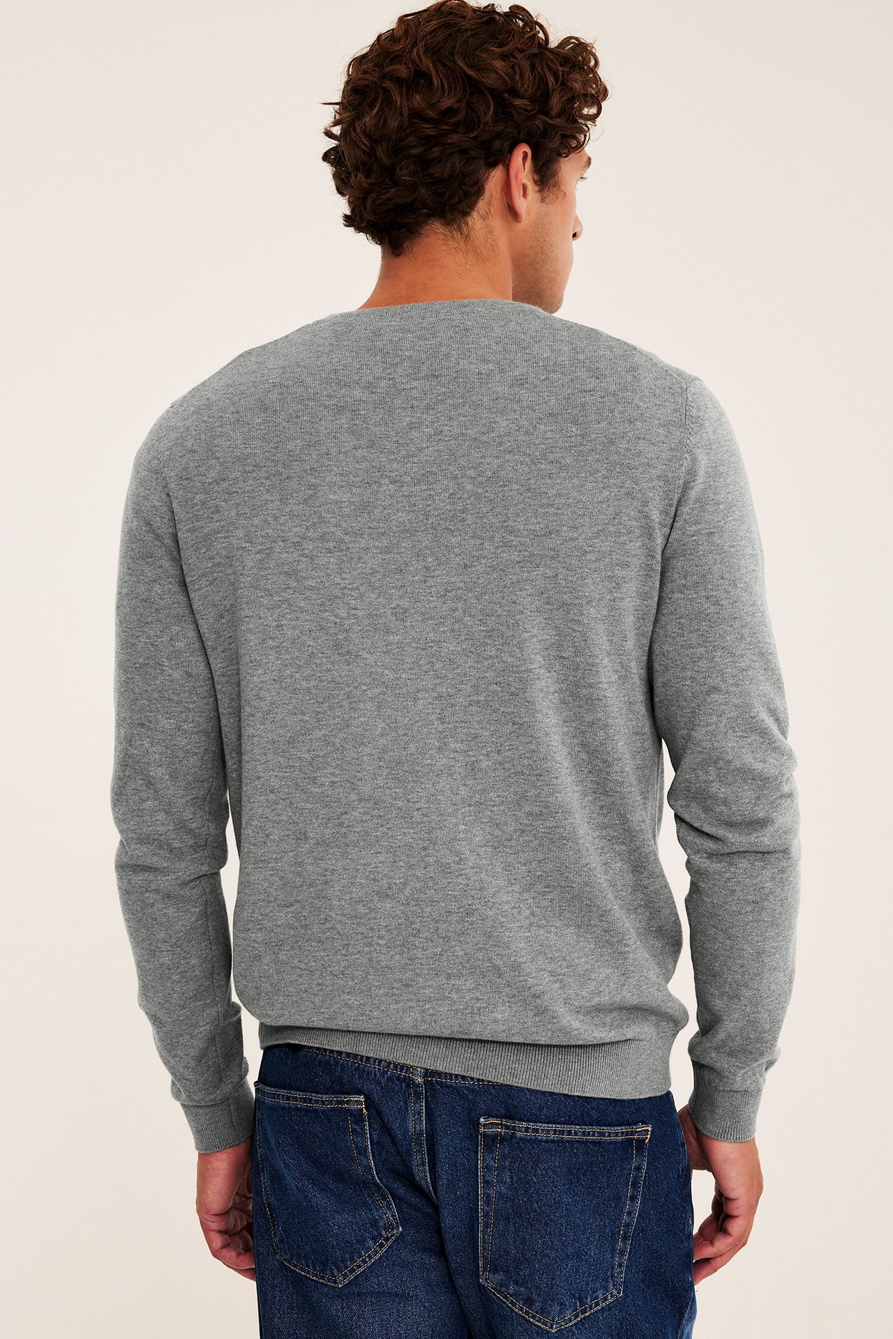 Ryggbild på en man i en grå långärmad tröja och blå jeans.