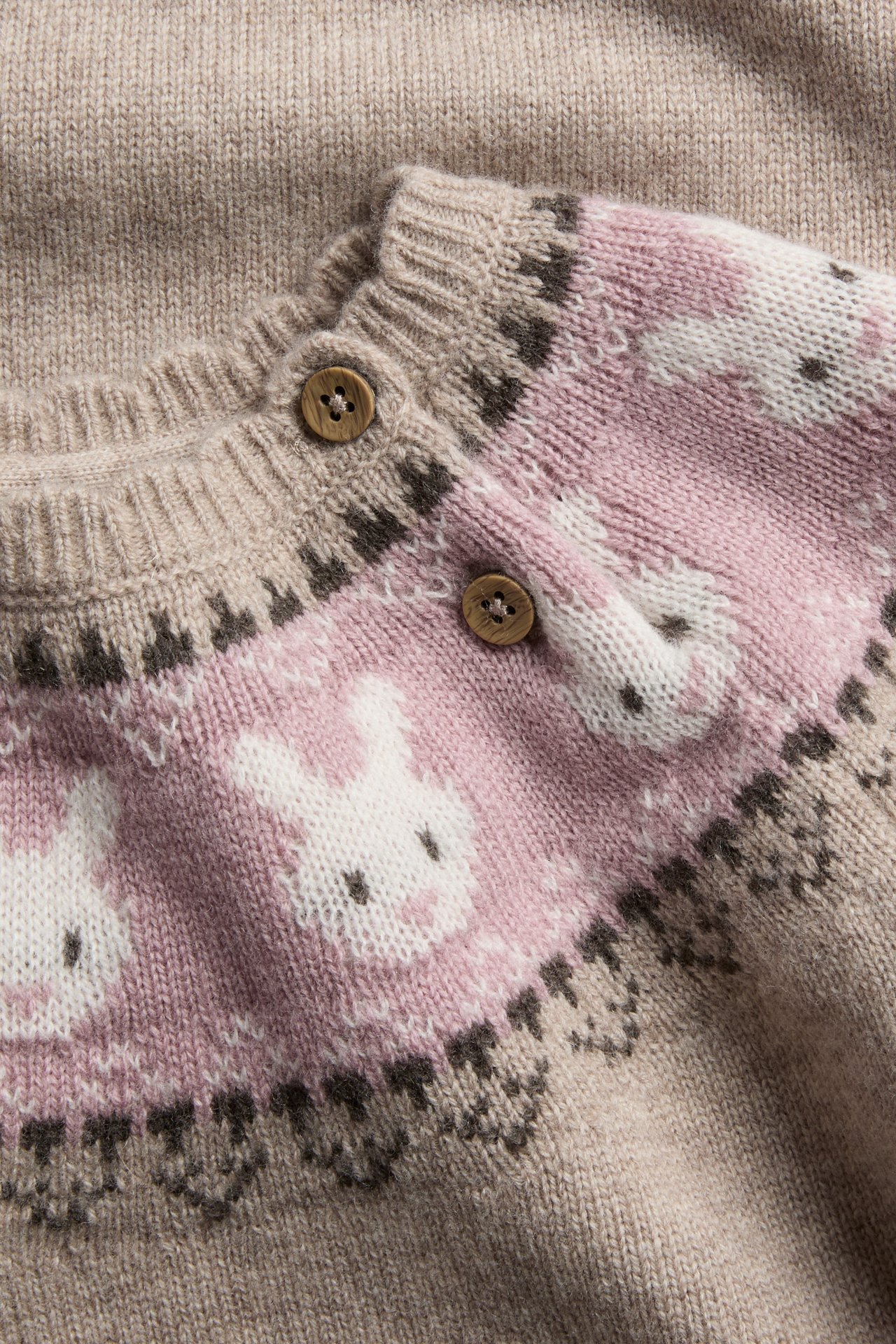 Lähikuva neulotusta lasten neuletakista, jossa beige pohja, pinkki pupukuvio ja ruskeat napit.