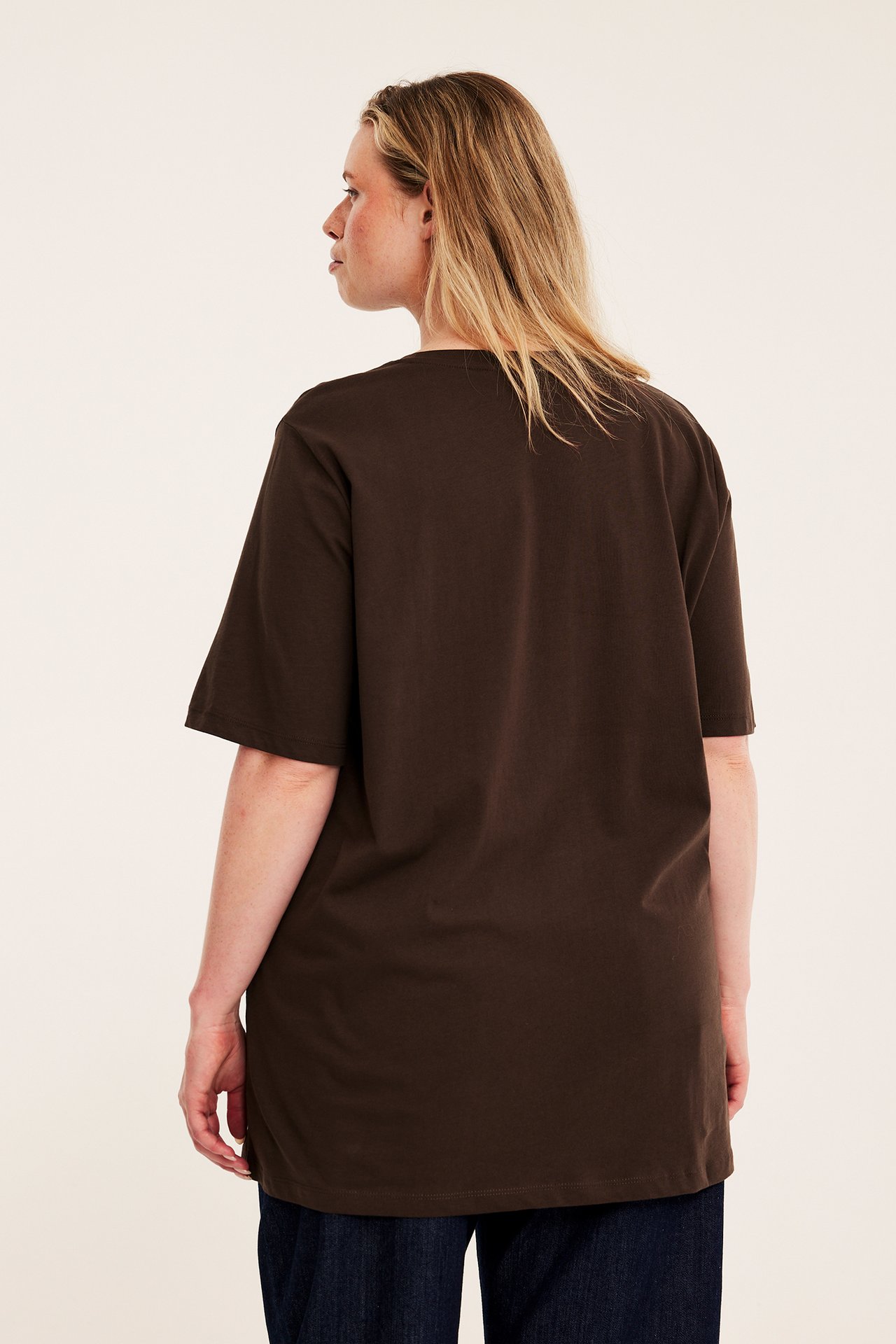 Voksen kvinne bakfra i mørkebrun oversized t-skjorte og mørkeblå jeans.