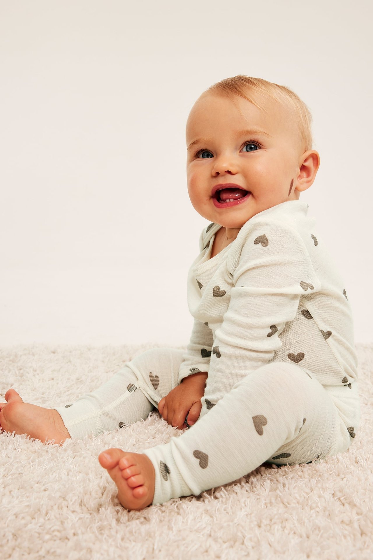 Edestä kuvattu vauva yllään kermanvärinen pyjama harmaalla sydänkuviolla.