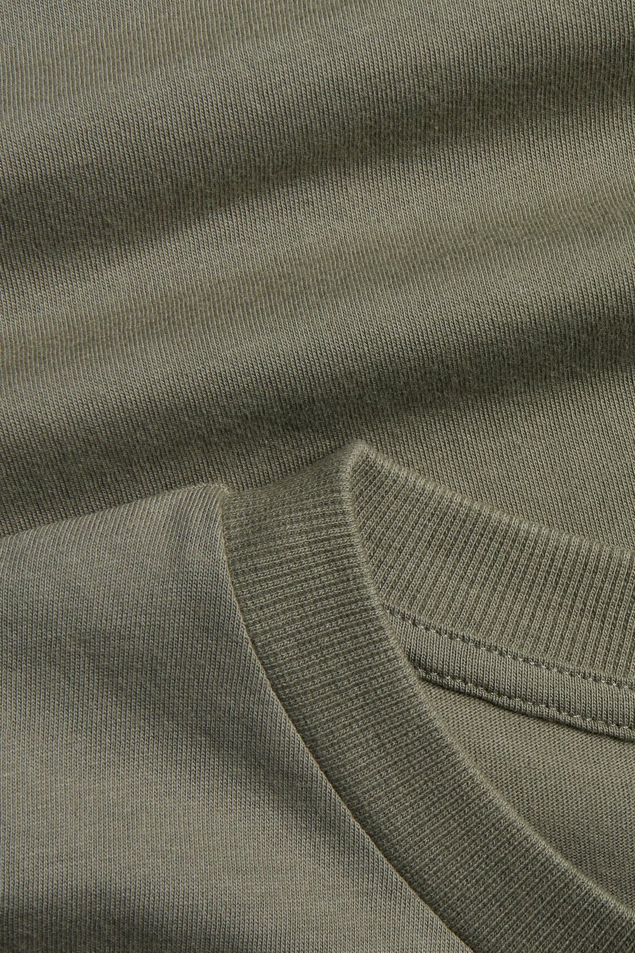 Zbliżenie ciemnozielonego T-shirtu z bawełnianej dzianiny z prążkowanym okrągłym dekoltem.