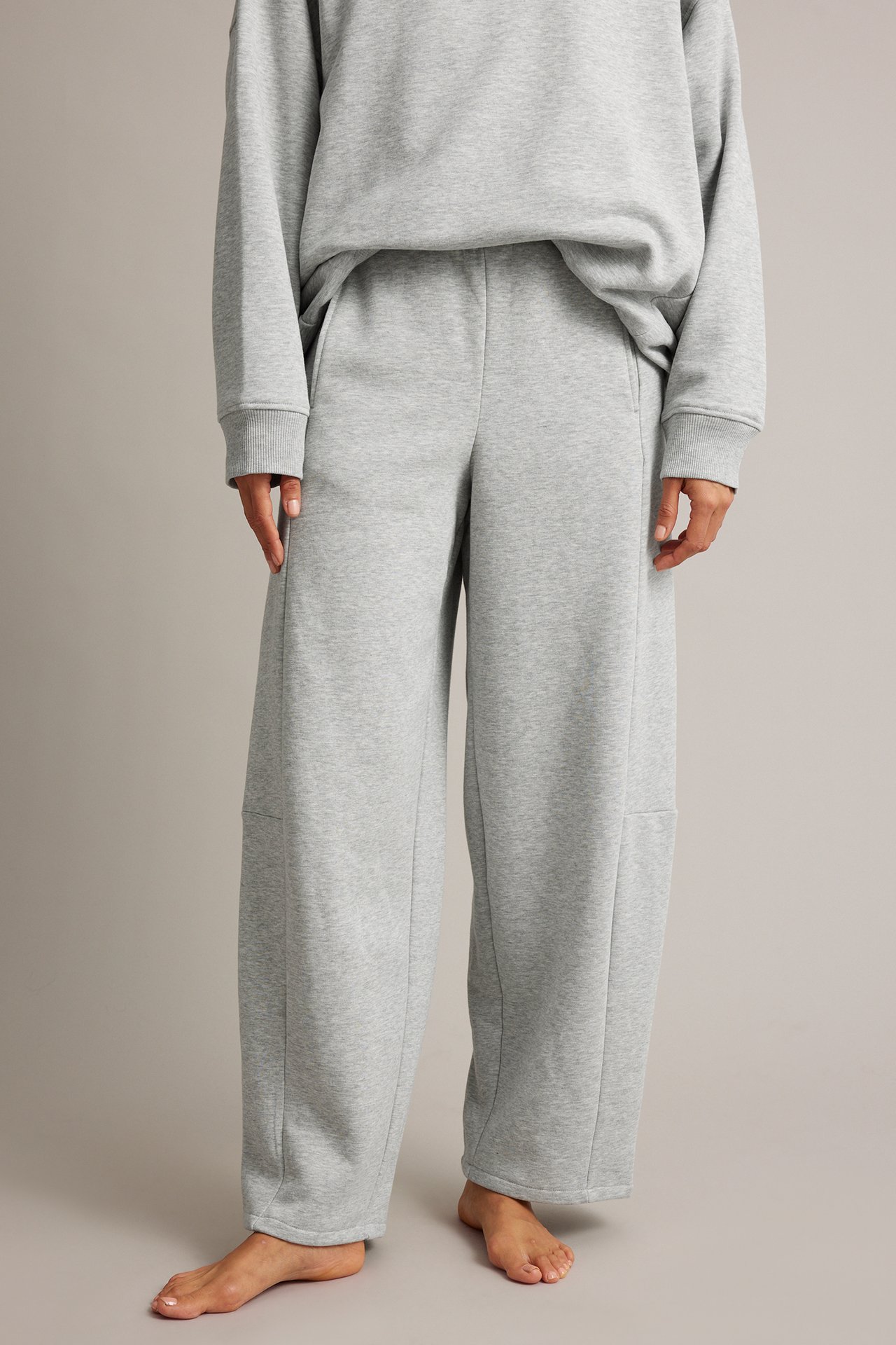Frontvy av kvinna i ljusgråmelerade wide-leg mjukisbyxor och matchande oversized sweatshirt.