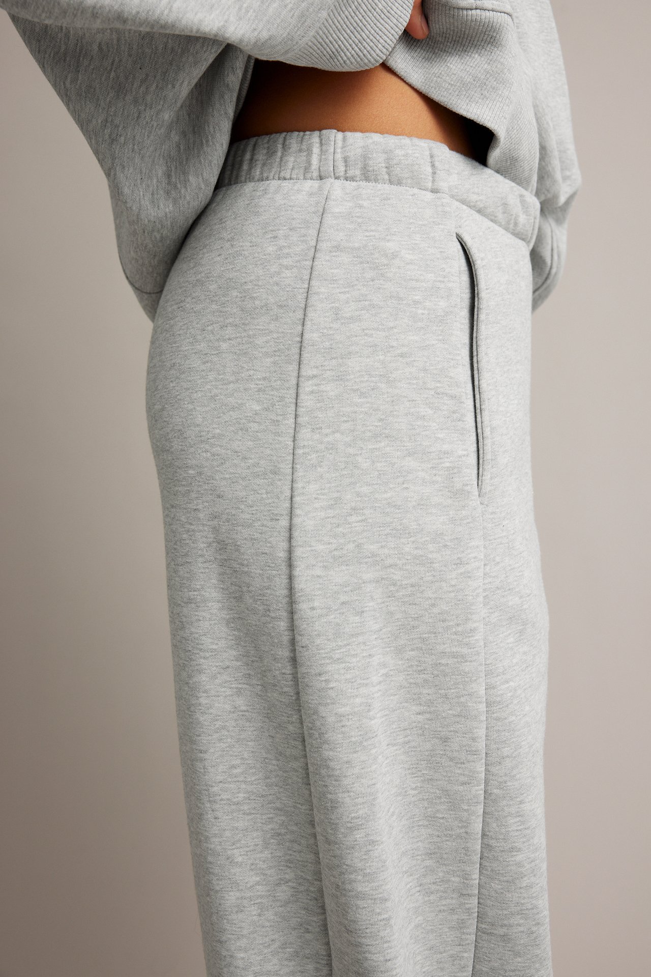 Sidovy av kvinnlig modell i gråmelerade sweatpants med matchande sweatshirt.