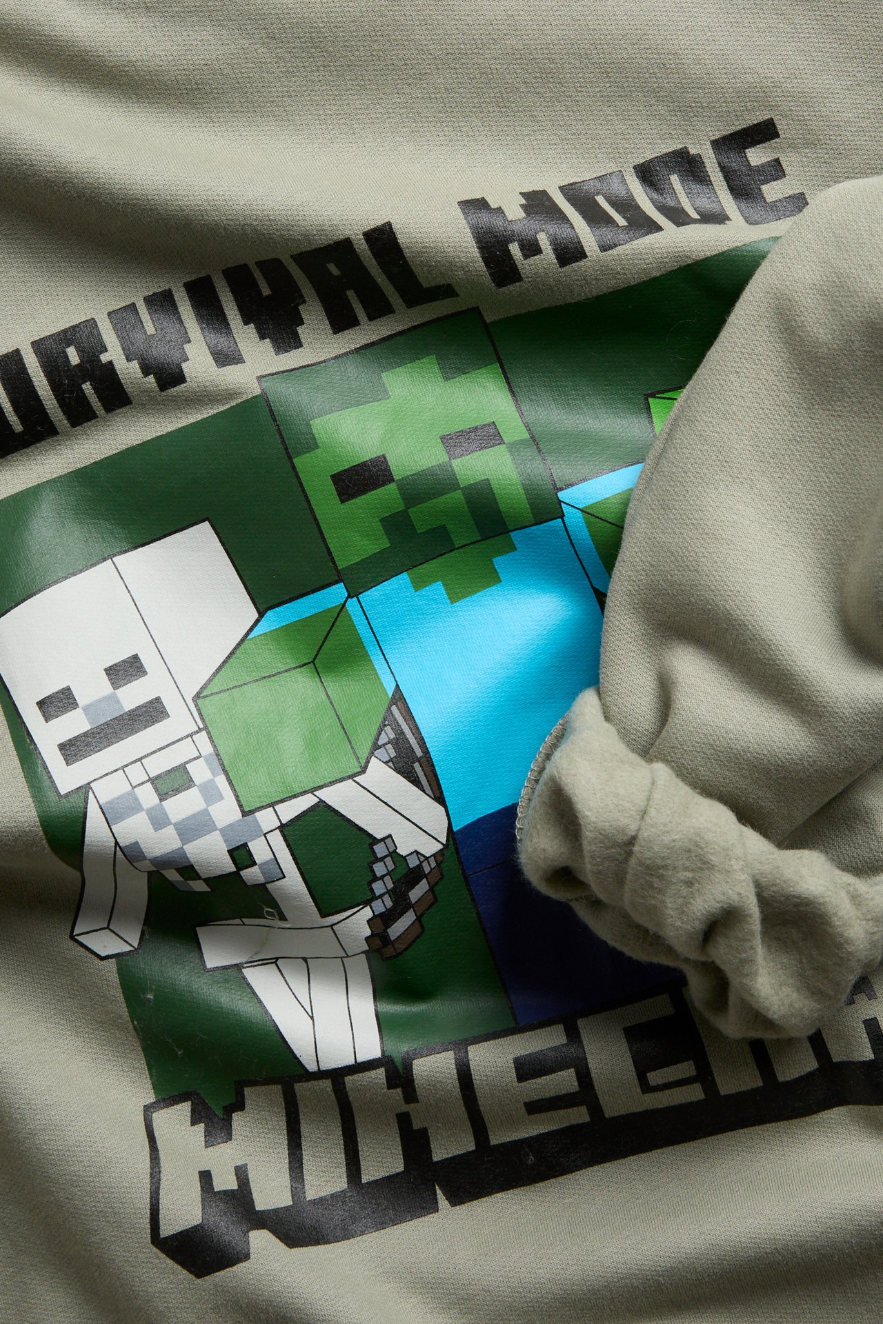 Lähikuva vaaleanvihreästä lasten pitkähihaisesta paidasta, jossa on Minecraft-hahmoja ja tekstipainatus.