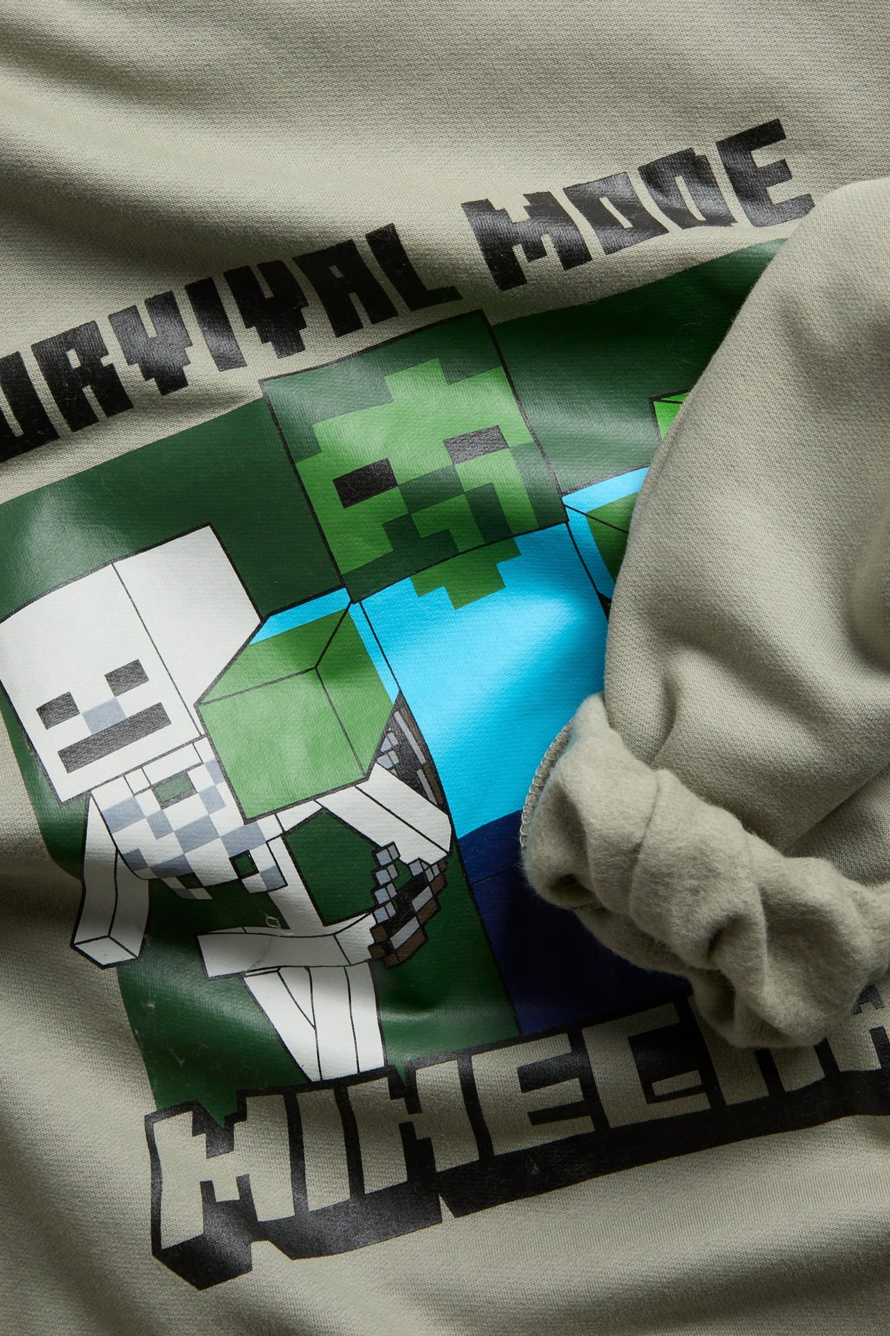 Zbliżenie na jasnozielony dziecięcy longsleeve z nadrukiem postaci i tekstu z Minecrafta.