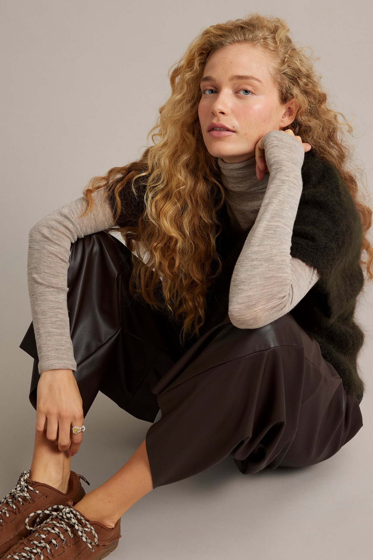 Front view, kvinna i mörkbruna culottes, beige polo, mörkgrön väst och bruna sneakers.
