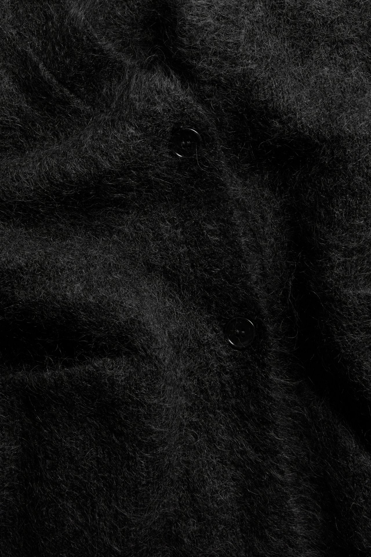 Zbliżenie na czarny puszysty kardigan z mieszanki moheru z dwoma widocznymi czarnymi guzikami.