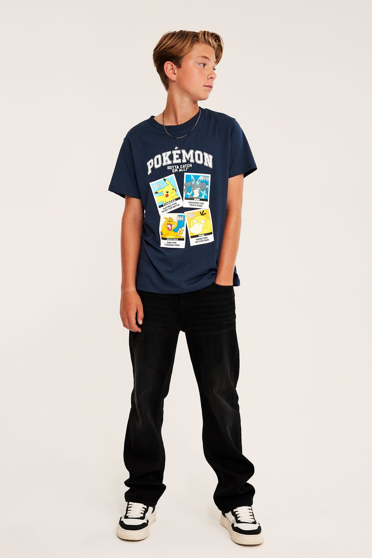 Hel frontvy av en mörkblå t-shirt med Pokémon-tryck för pojke, svarta jeans och vita och svarta sneakers.