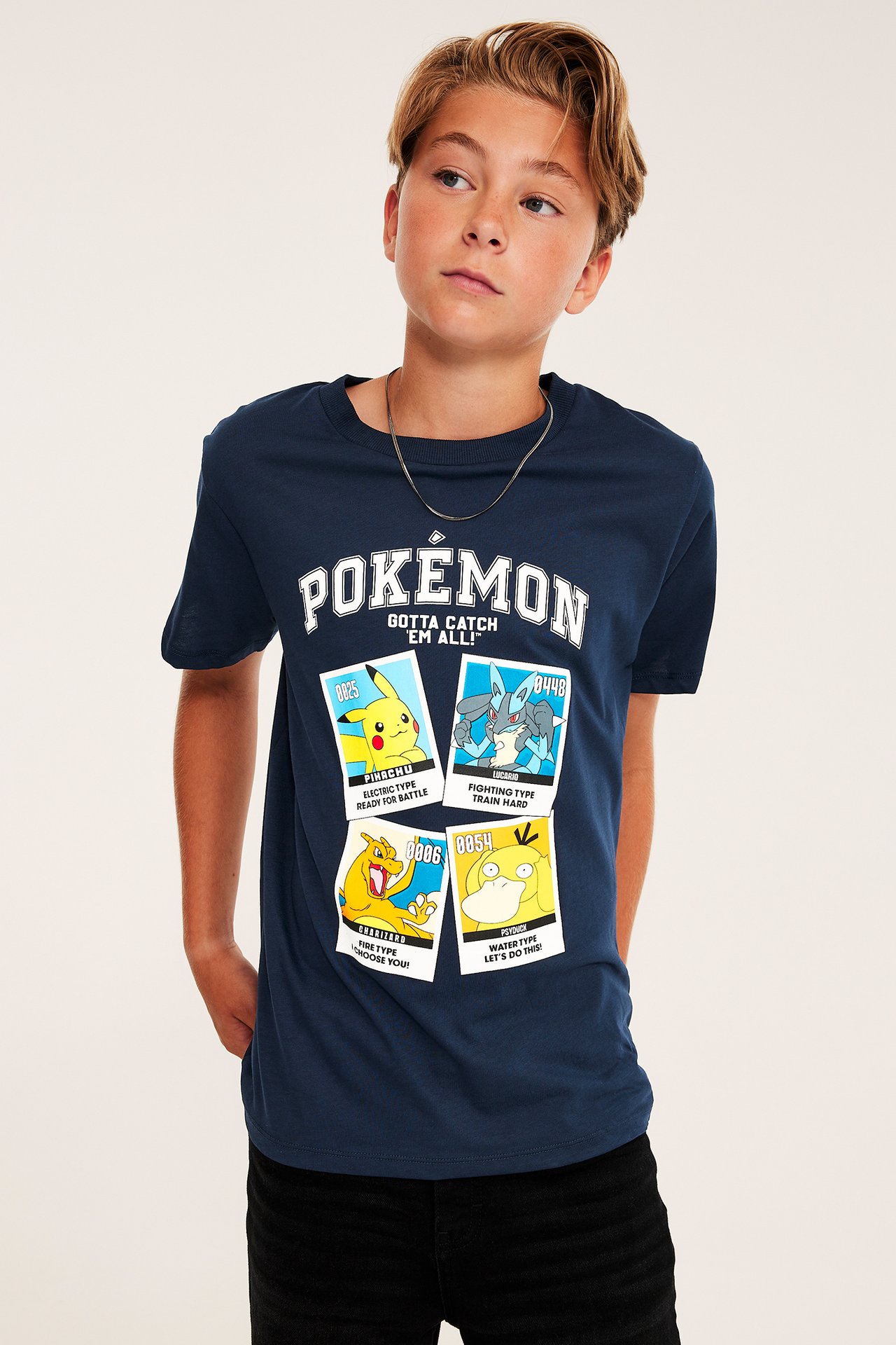 Widok z przodu, chłopiec w granatowej koszulce Pokemon z nadrukiem, czarnych spodniach i srebrnym łańcuszku.