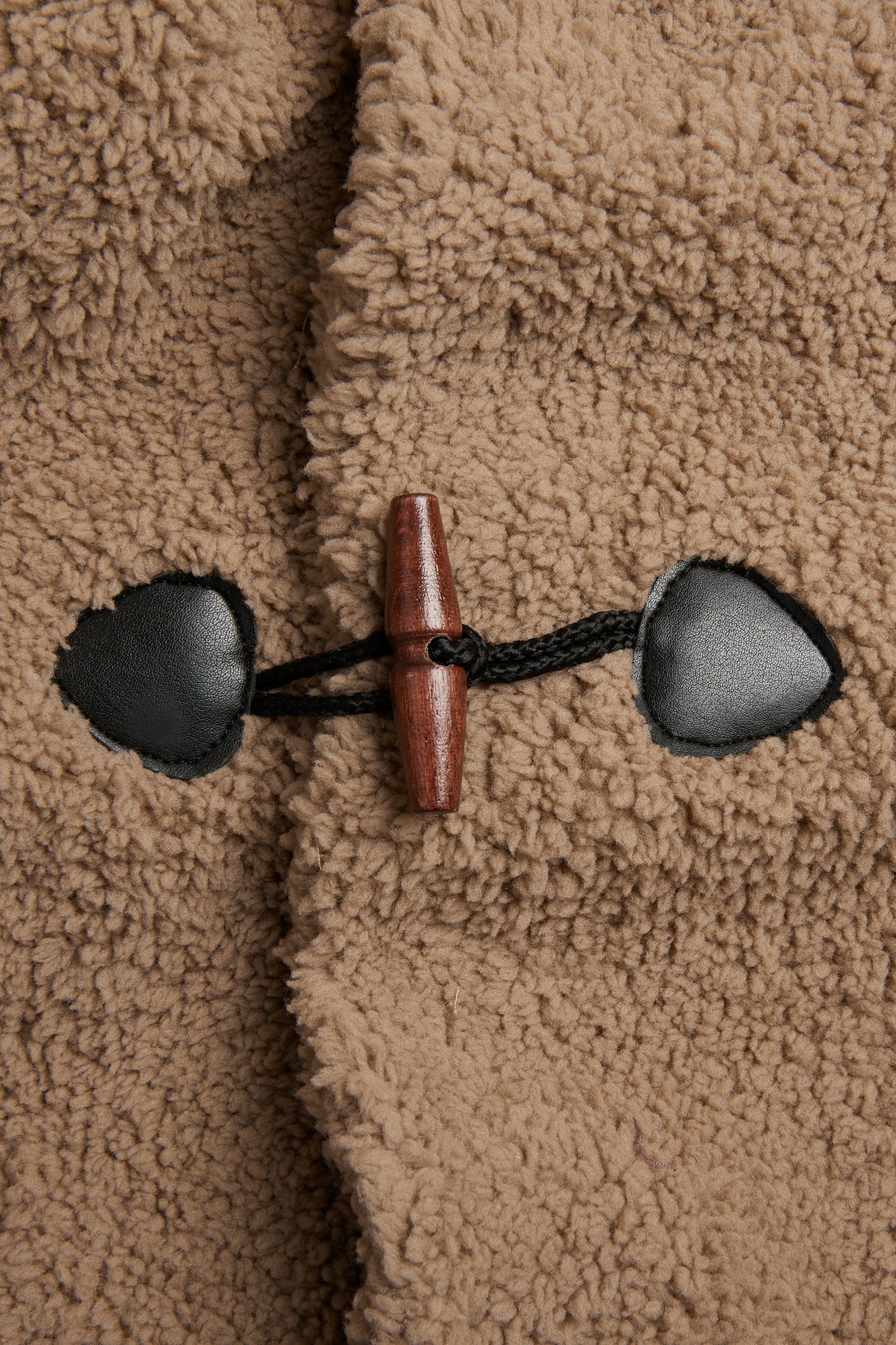 Lähikuva beigestä fleecetakista, jossa puinen duffelinappi ja mustat tekonahkasilmukat.