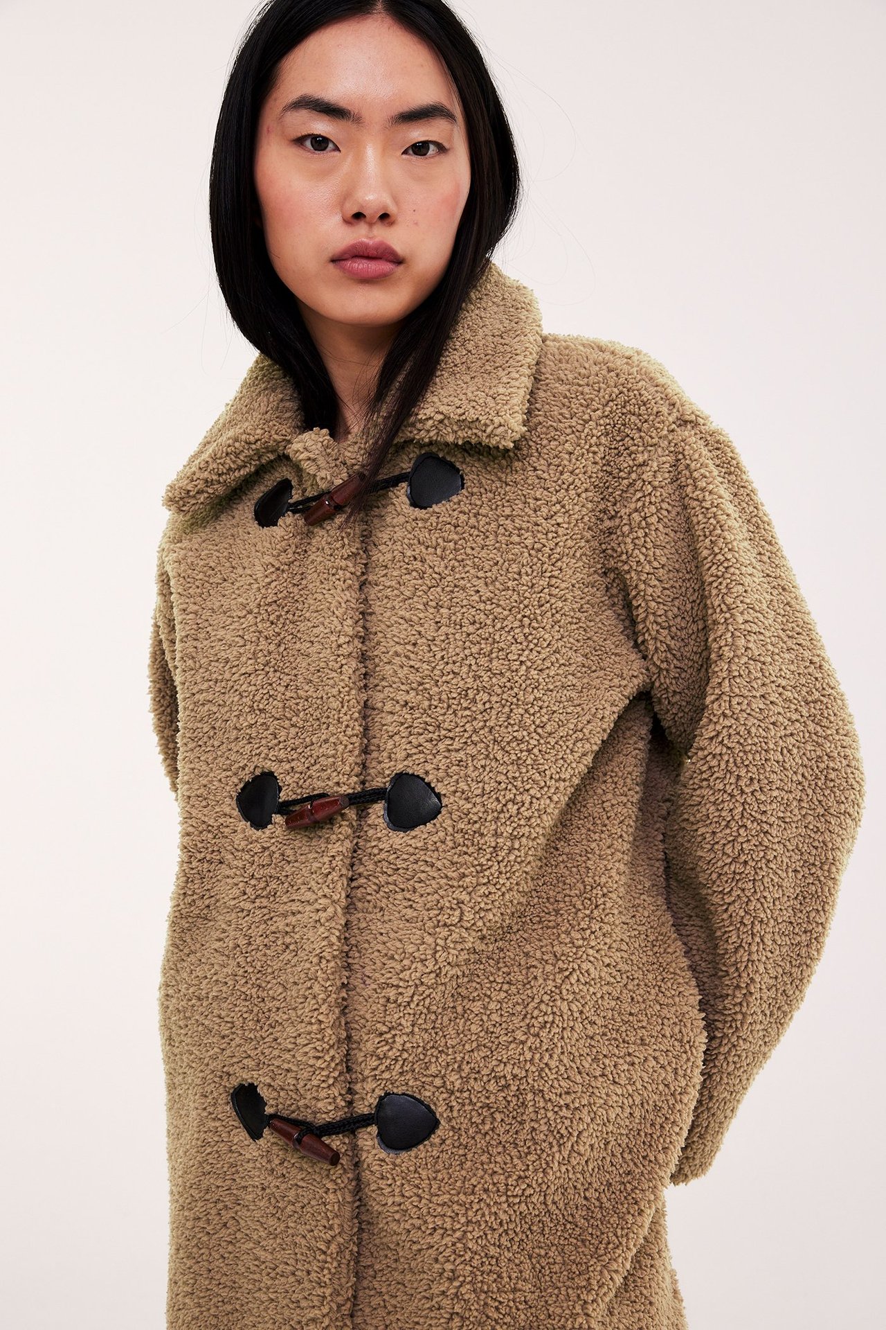 Framifrån: kvinna i beige pilejacka med duffelknappar i läderimitation.