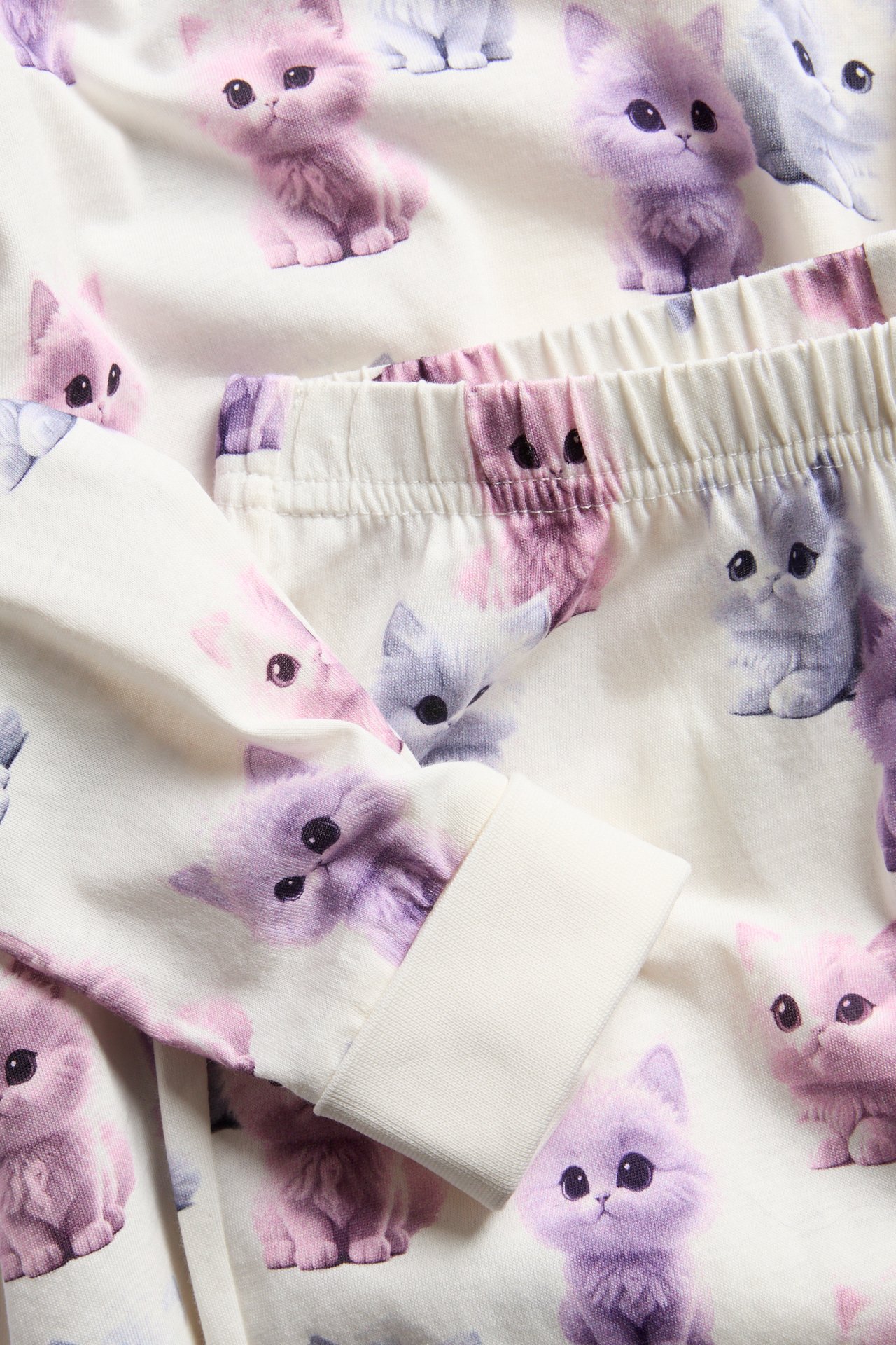 Närbild på vita barnpyjamasbyxor med färgglatt kattryck, resår i midjan och muddar.