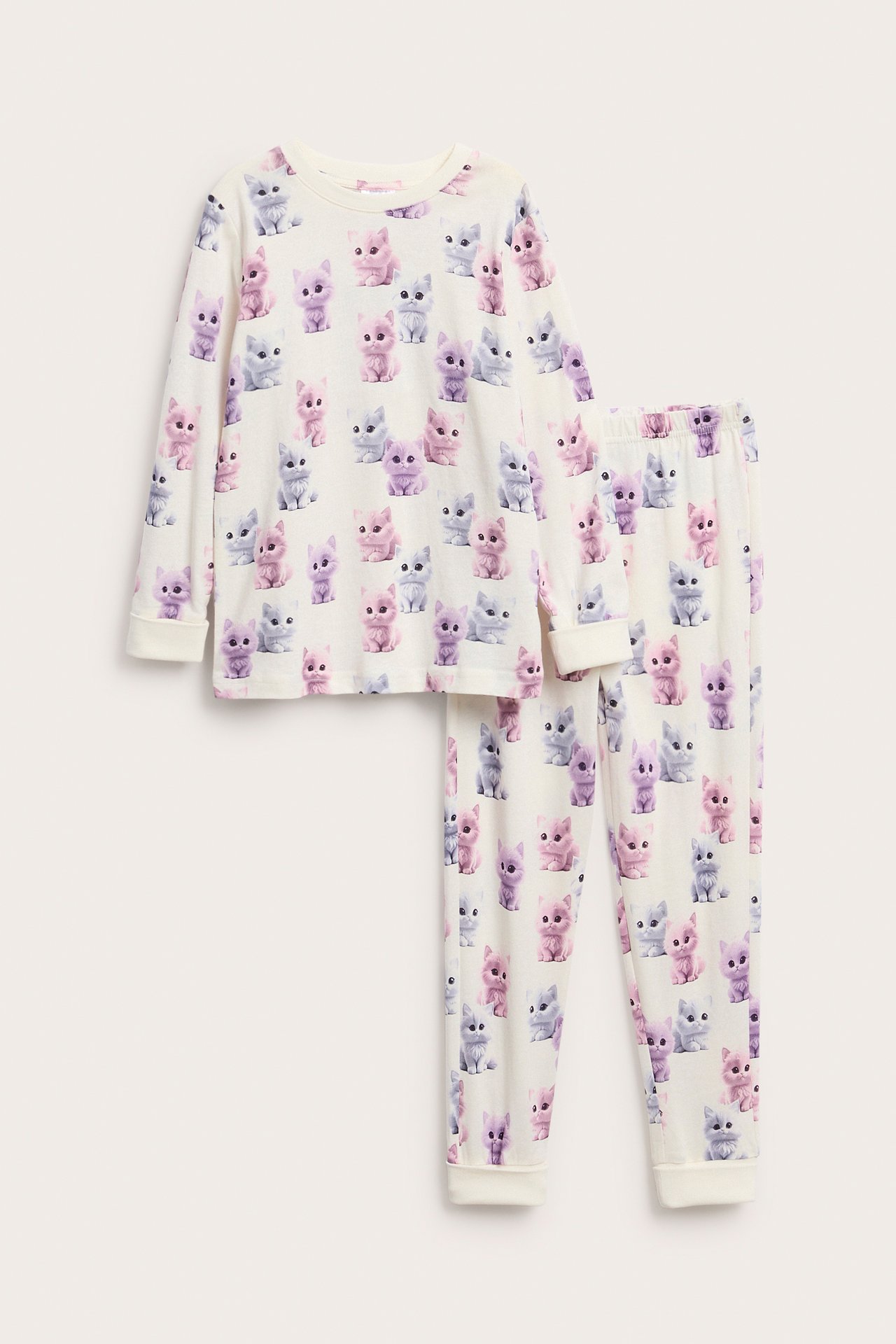 Framifrån, ett barns pyjamas med långa ärmar i krämvitt med färgglatt kattmönster.