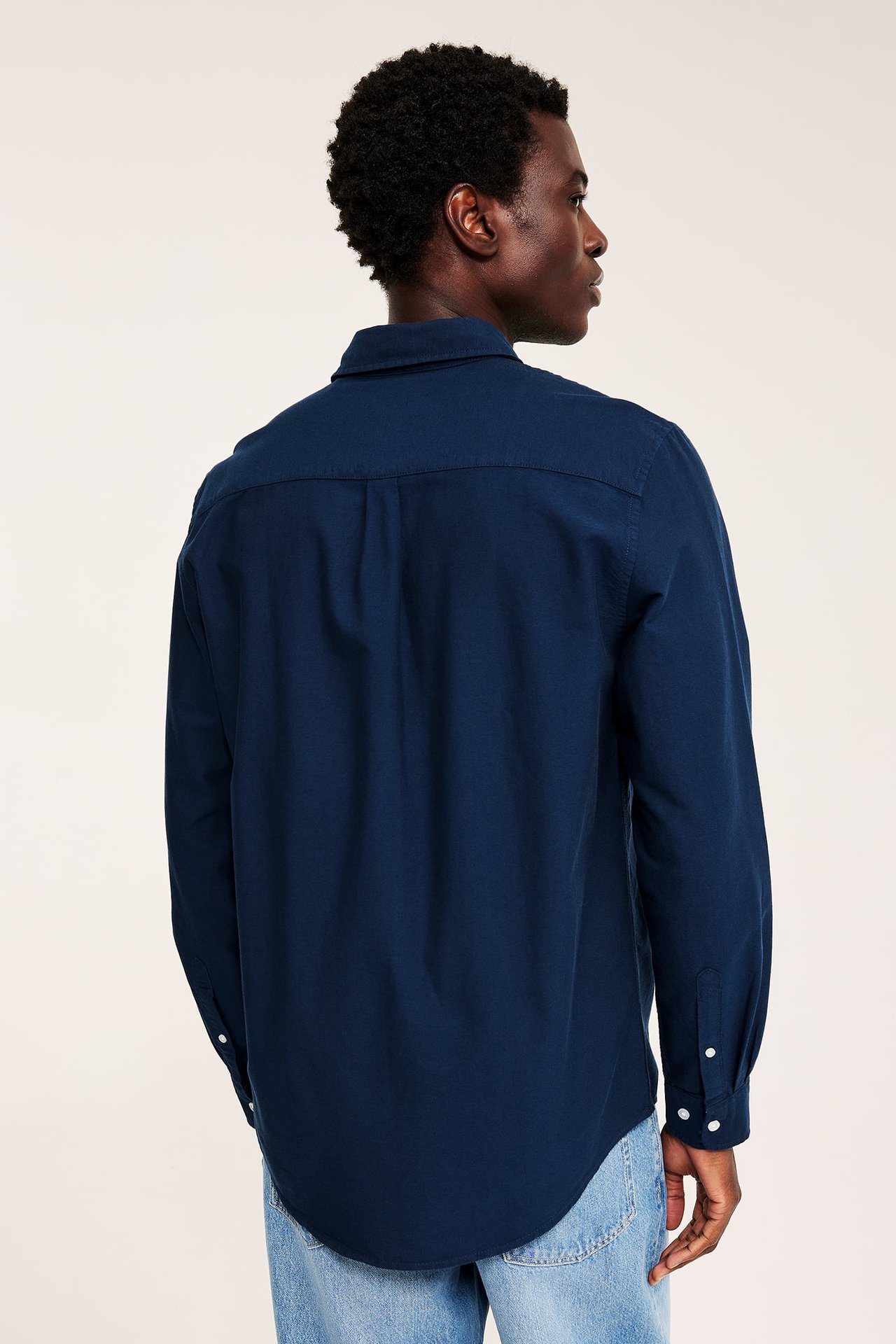Bakfra, mann i mørkeblå langermet skjorte og lyseblå jeans.