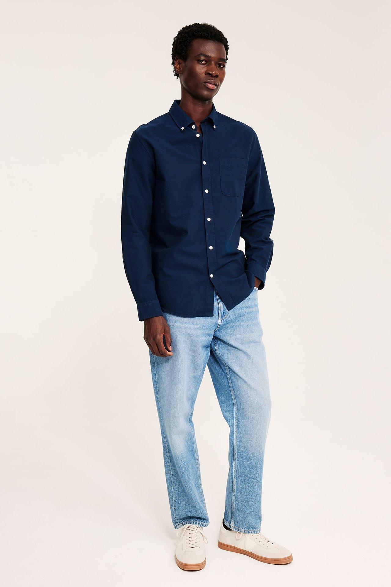 Mørkeblå langermet skjorte på mann med lyseblå jeans og beige joggesko.