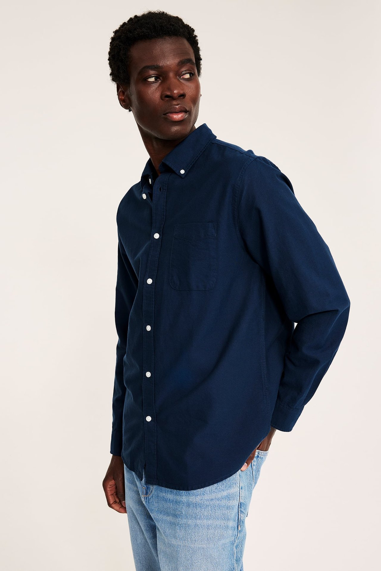 Skrått forfra-bilde av en voksen mann iført en marineblå langermet button-down-skjorte og lyseblå jeans.