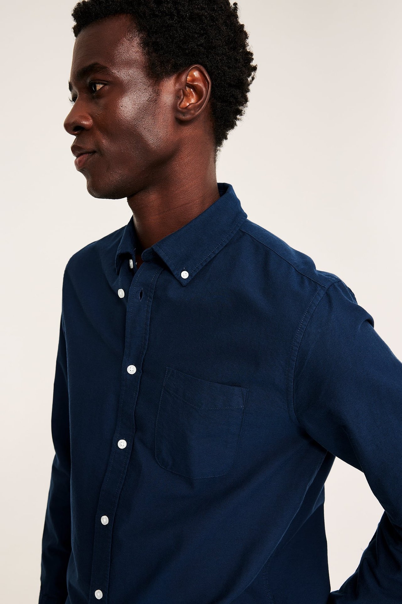 Sidebilde av en voksen mann i en mørk blå langermet button-down-skjorte med brystlomme.