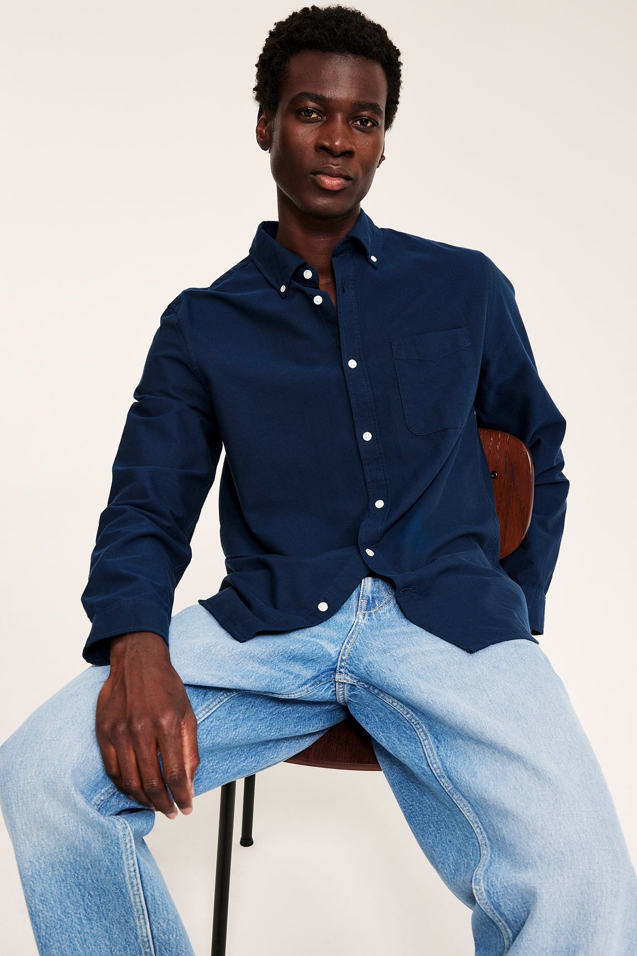 Frontbilde av en mann i mørkeblå langermet skjorte og lyseblå vidbeinte jeans.
