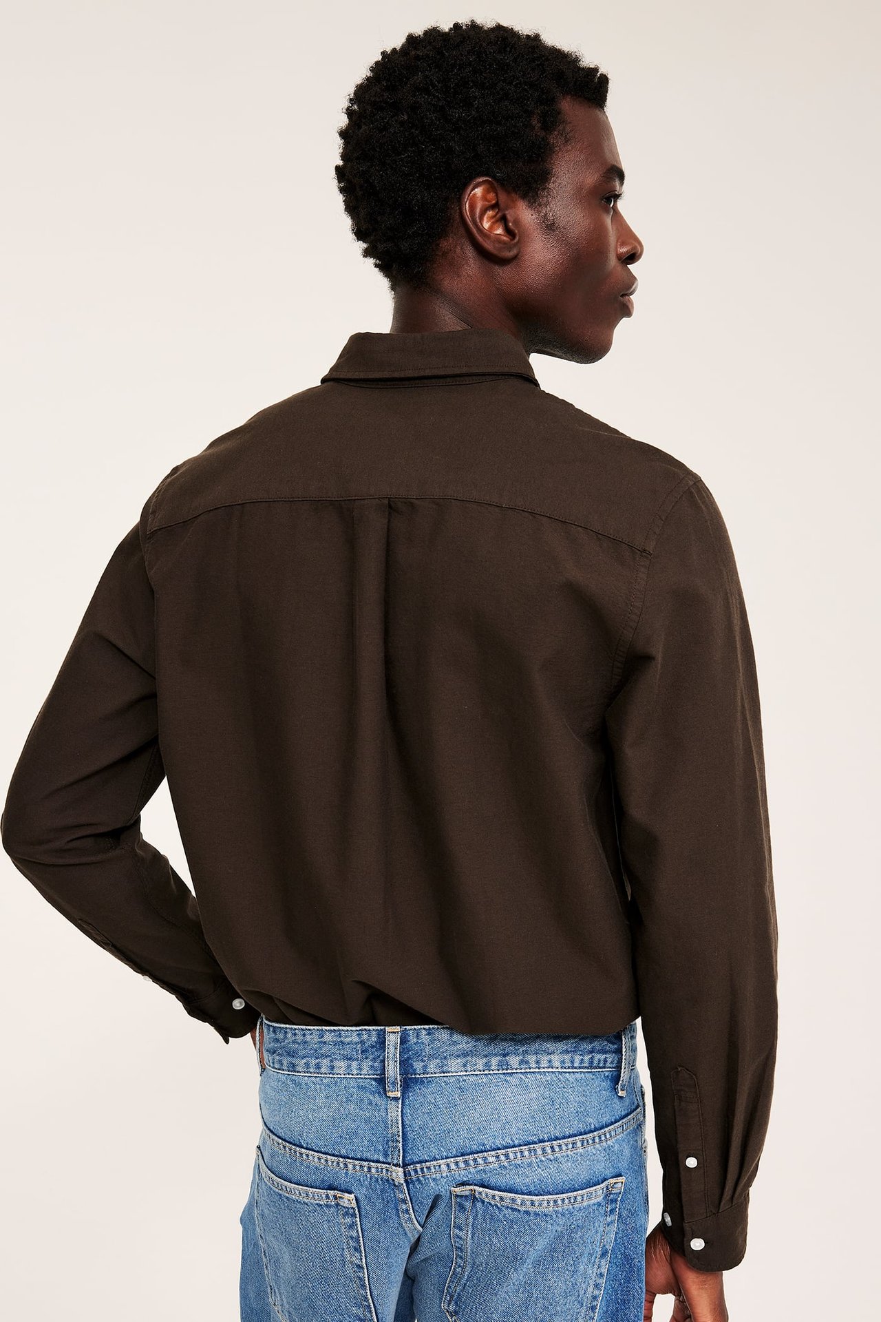 Bakfra av en mannlig modell iført en mørkebrun langermet skjorte og blå jeans.