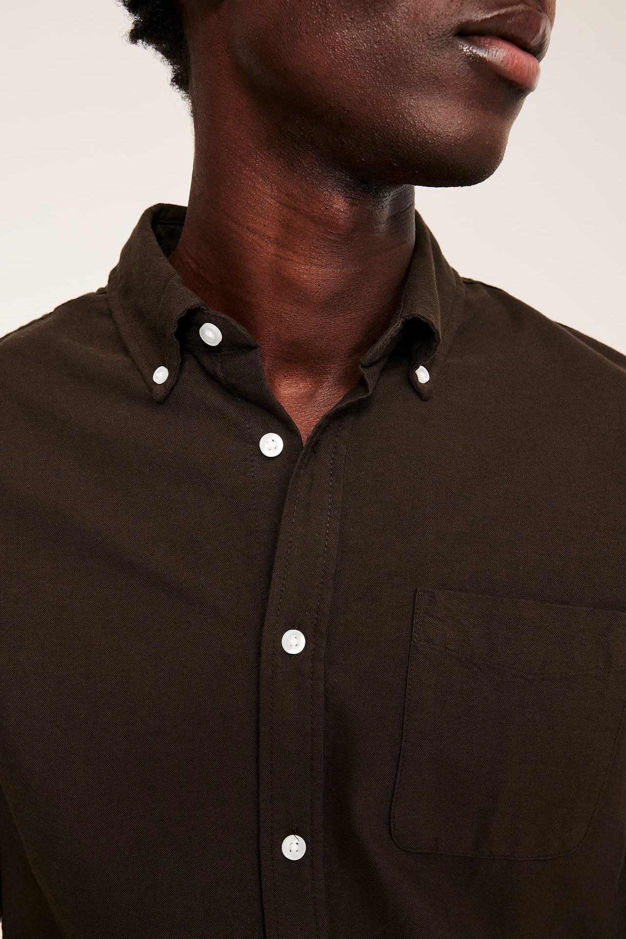 Nærbilde av mann i mørkebrun skjorte med hvite knapper og button-down krage.