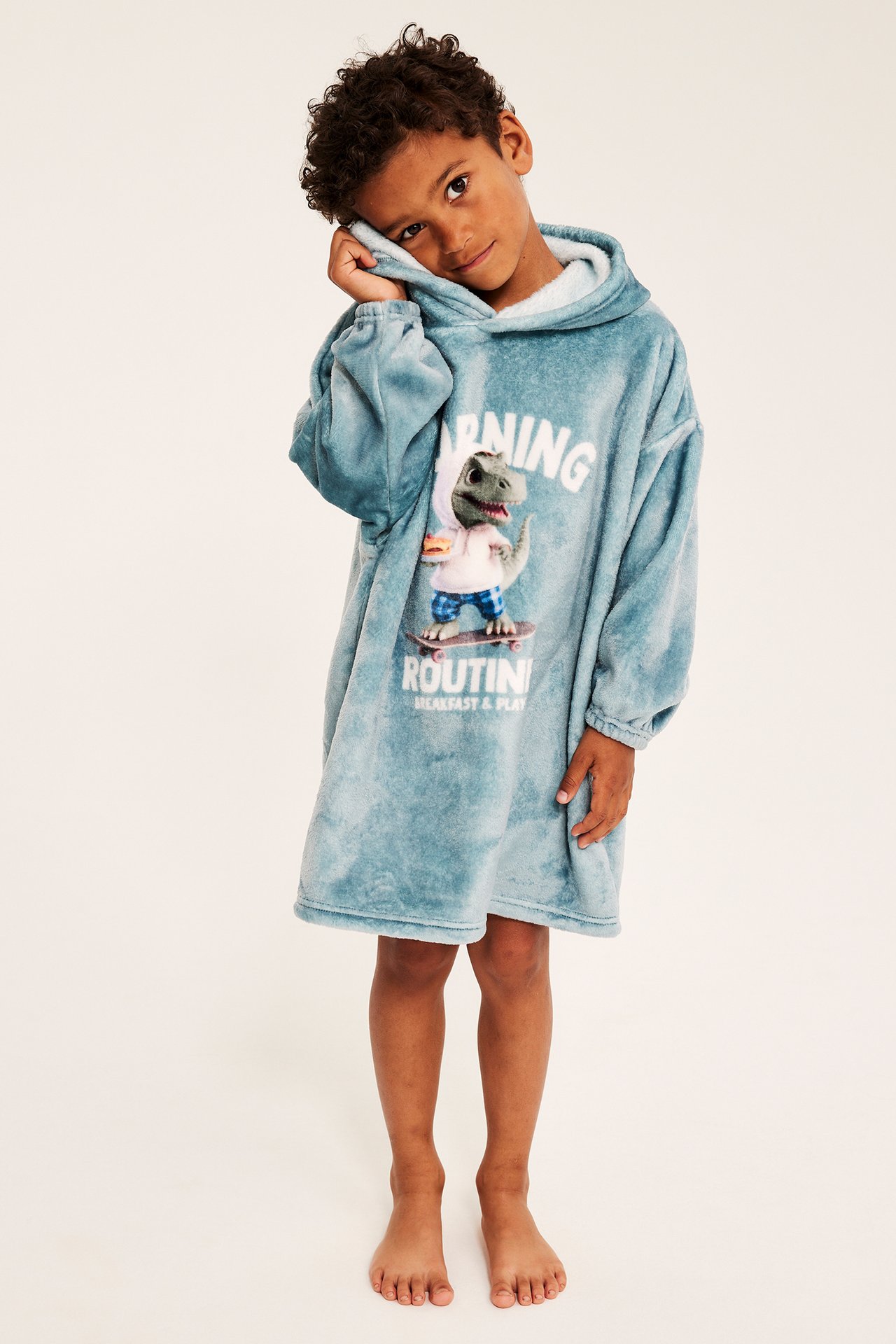 Framifrån, barn i blå fleece oversized huvtröja-filt med dinosauriemotiv.