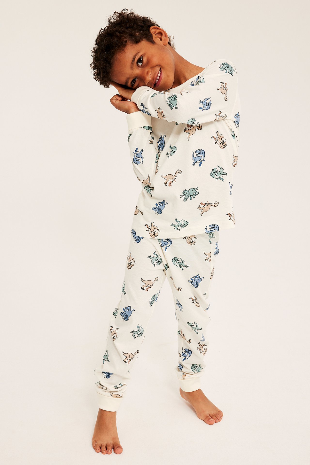Frontvy av ett barn i offwhite långärmad pyjamas med färgglatt dinosauriemönster.