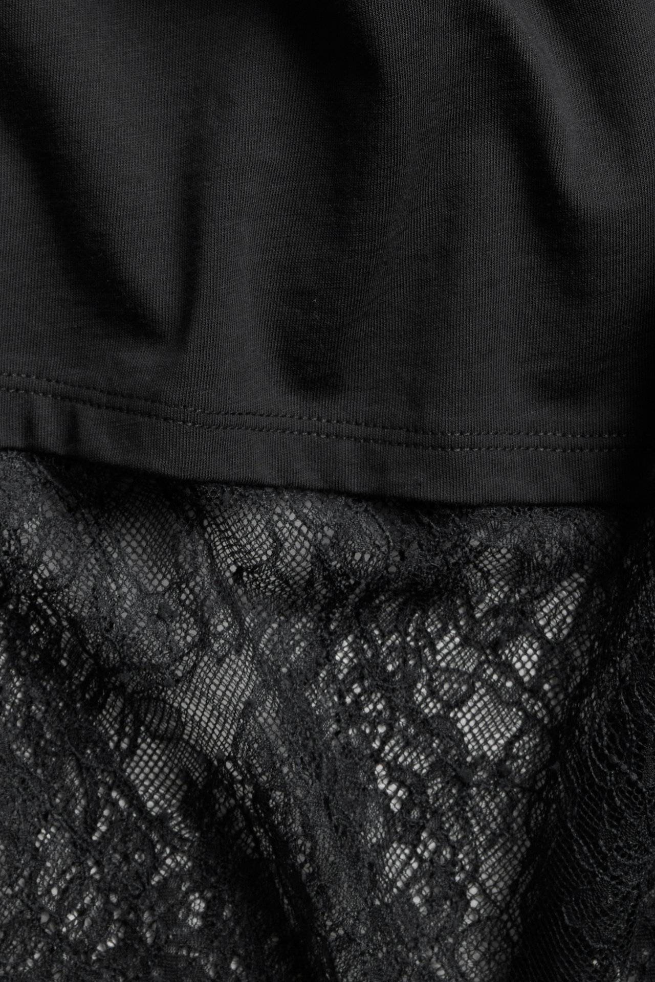 Lähikuva mustasta löysästä T-paidasta, jossa on leveä, yksityiskohtainen musta pitsireuna.