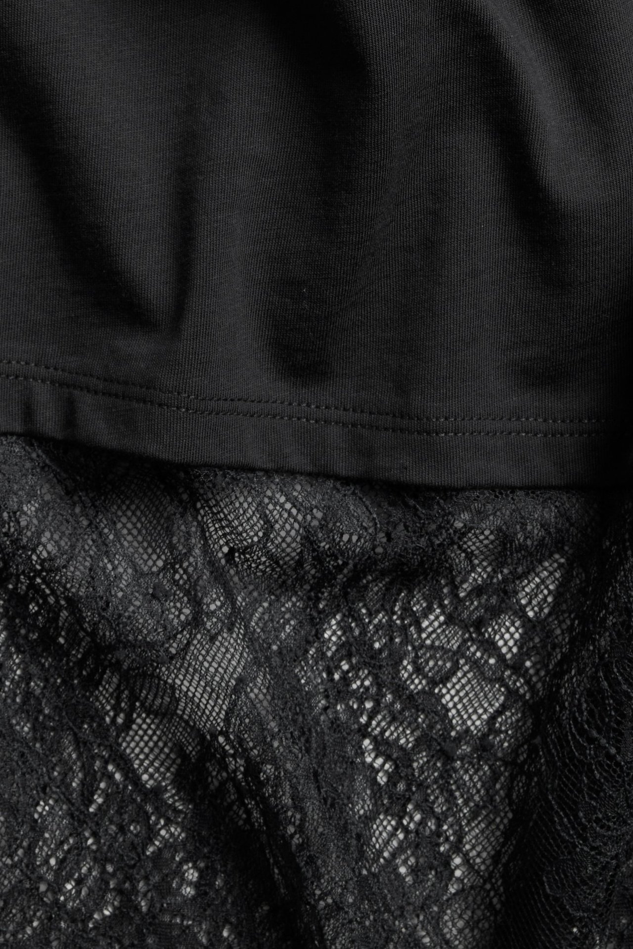 Zbliżenie czarnego, luźnego T-shirtu z szerokim, szczegółowym czarnym koronkowym dołem.