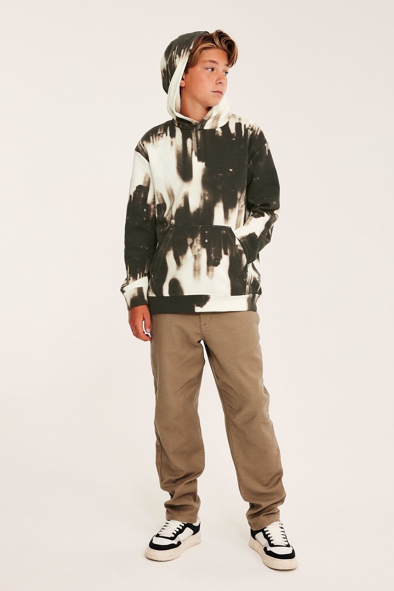 Frontbilde av et barn i svart-hvit tie-dye hettegenser, brune bukser og svarthvite sko.