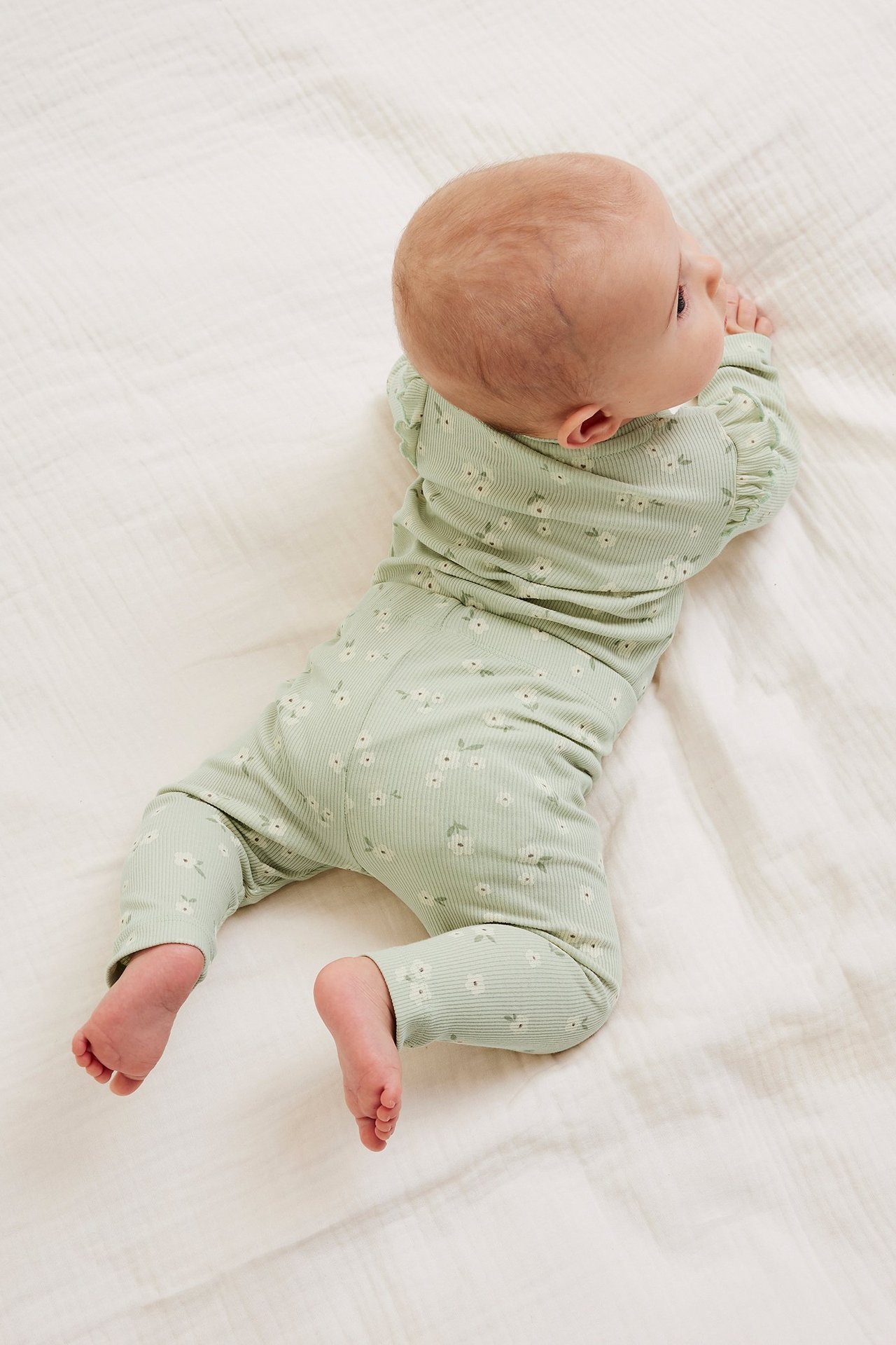 Widok z góry: niemowlę w jasnozielonych prążkowanych legginsach w kwiaty i pasującej górze.