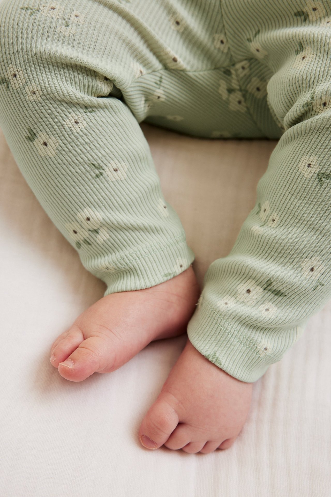 Lähikuva vauvan jaloista, yllään vaaleanvihreät ribatut kukkakuosiset leggingsit ja paljaat jalat.