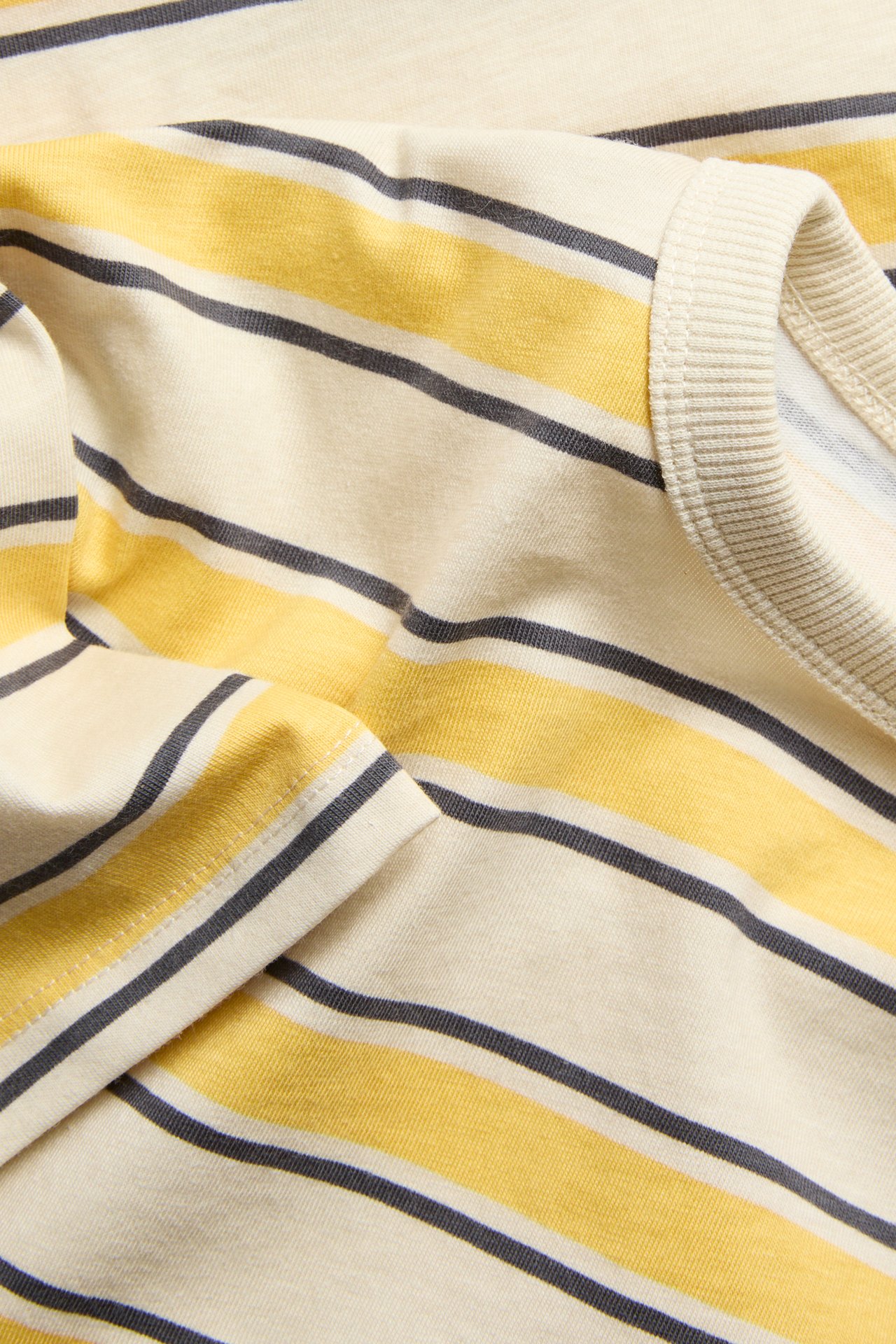 Nærbilde av bomull t-skjorte med gule, lys beige og mørkegrå striper, ribbet krage.