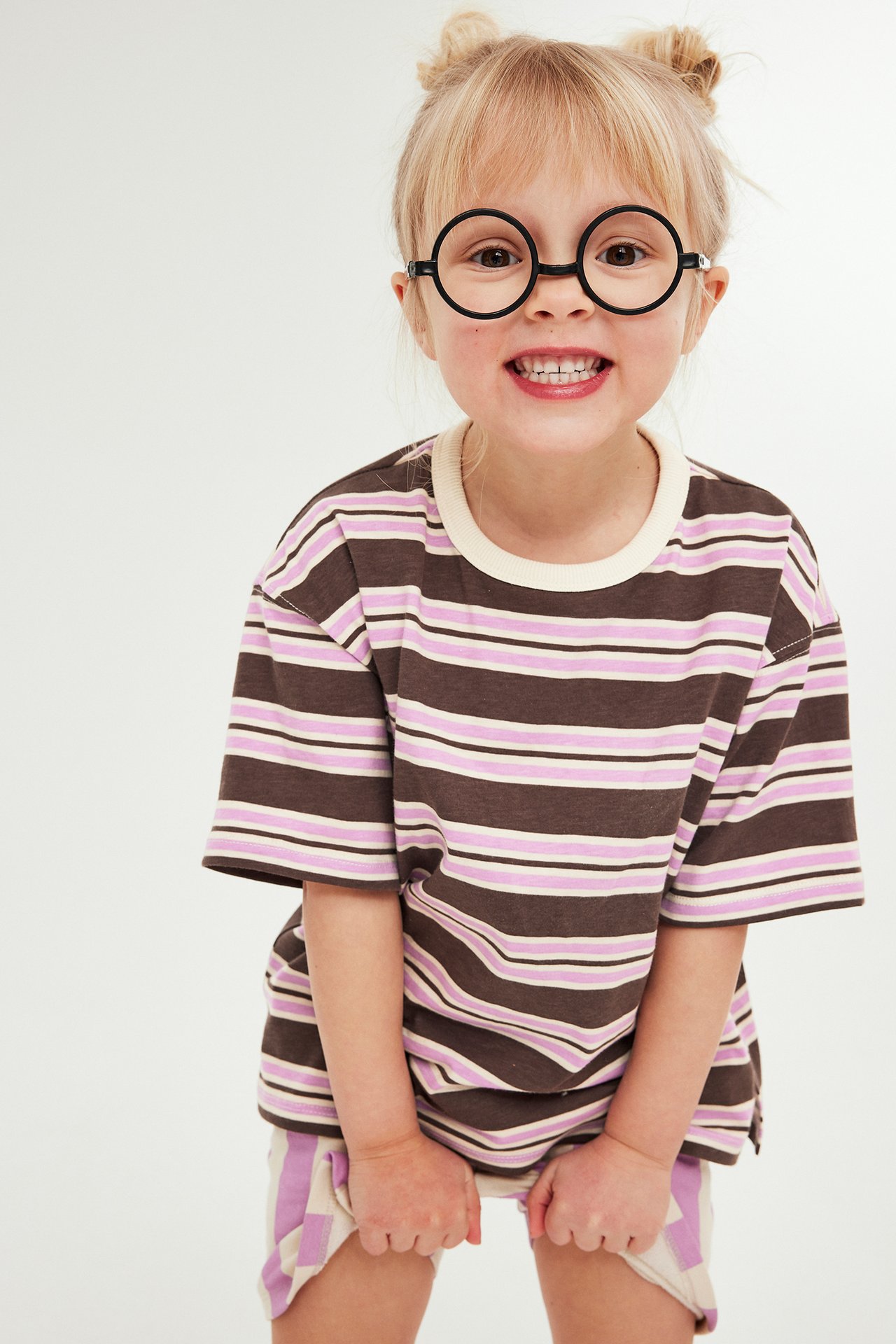 Forfra: Barn i brun, rosa og hvitstripet t-skjorte, matchende shorts og runde svarte briller.
