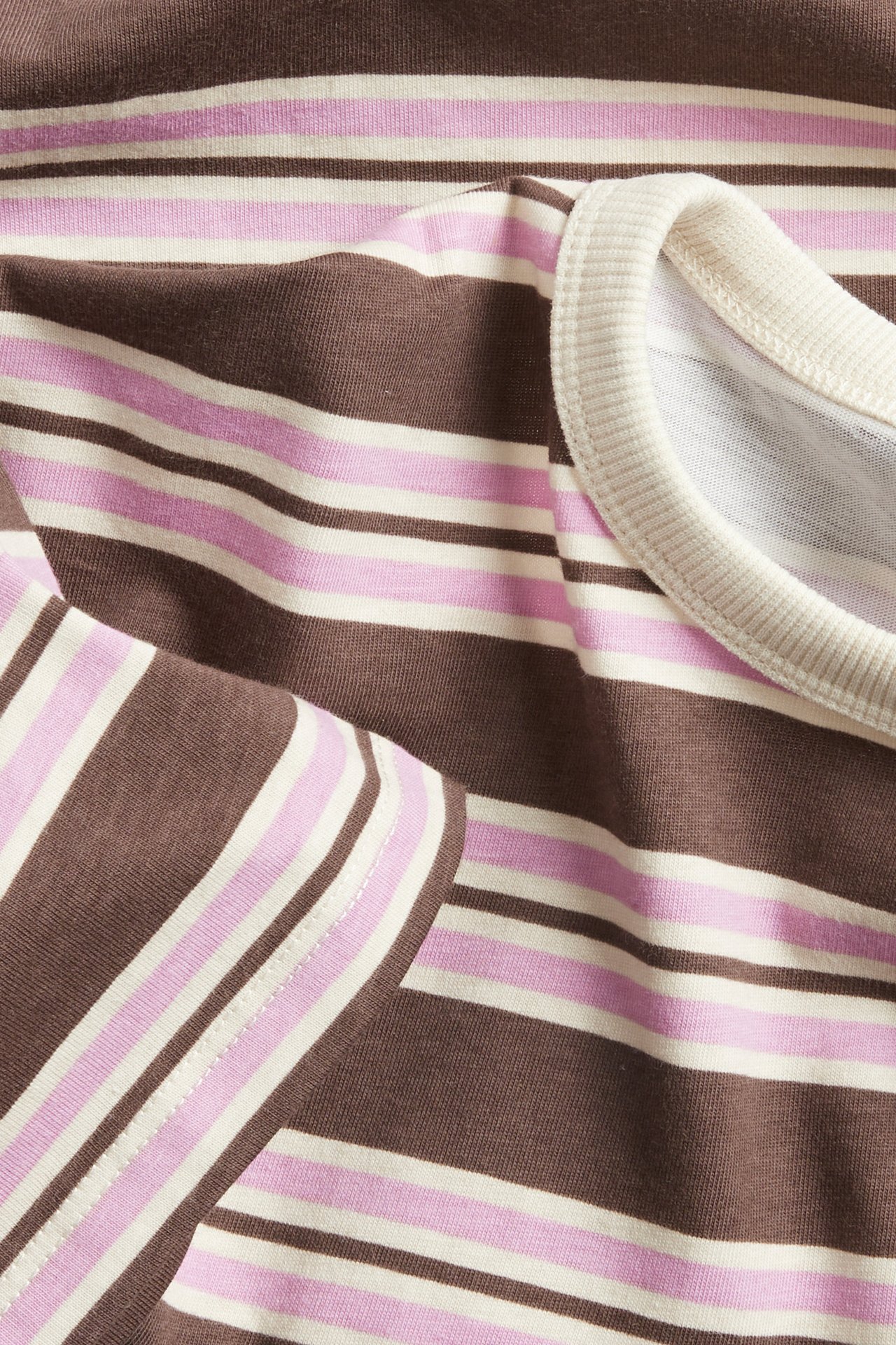 Nærbilde av en brun, rosa og kremfarget stripet T-skjorte i bomull med ribbet rund hals.