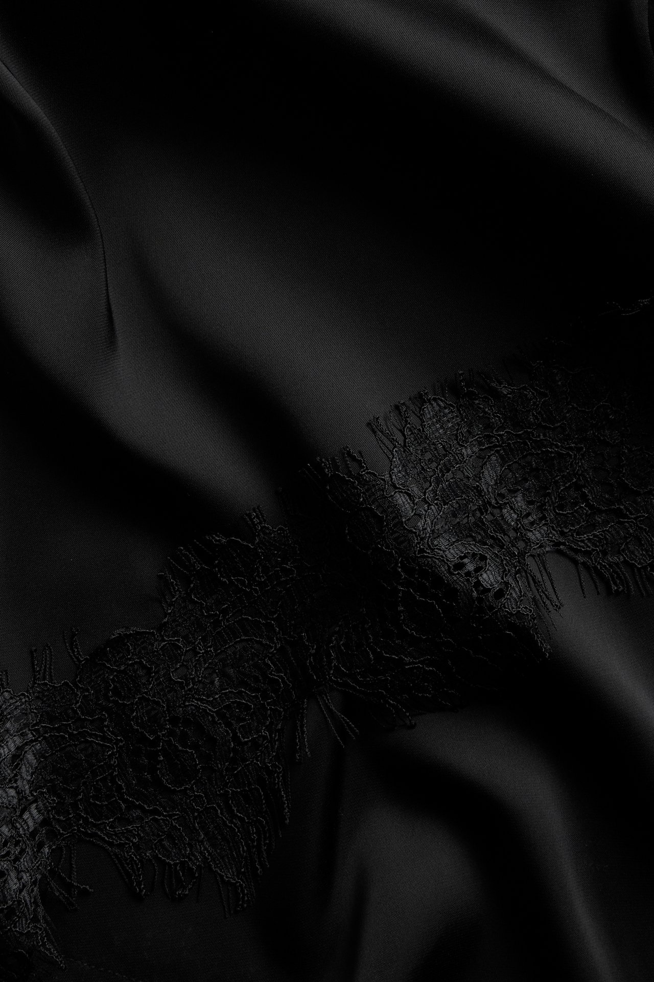 Lähikuva mustasta satiinimekosta, jossa on herkkä musta pitsireunus helmassa.