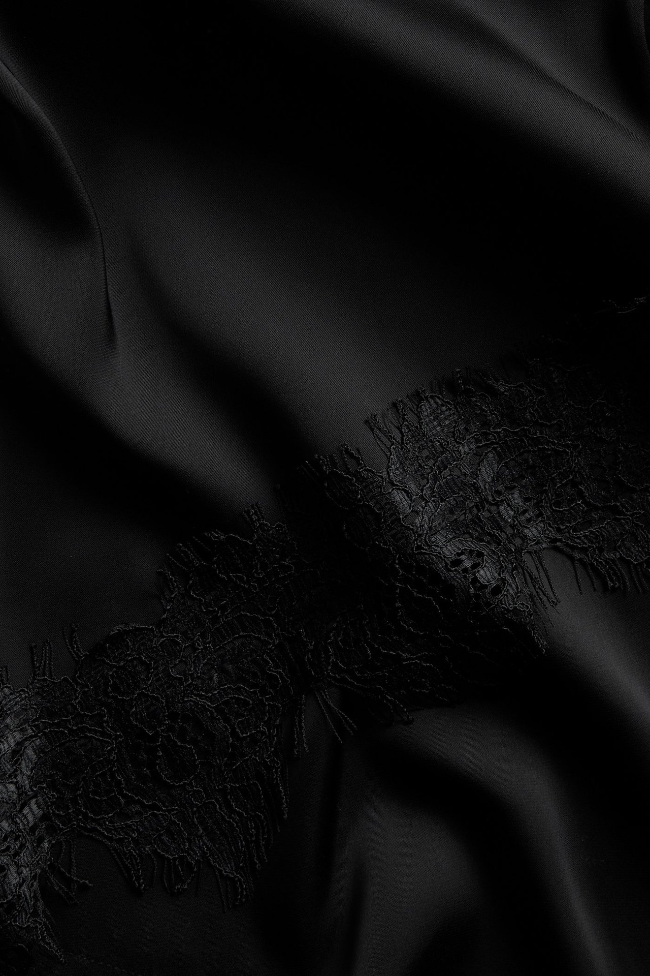Närbild av en svart satinklänning med delikat svart spetskant nedtill.