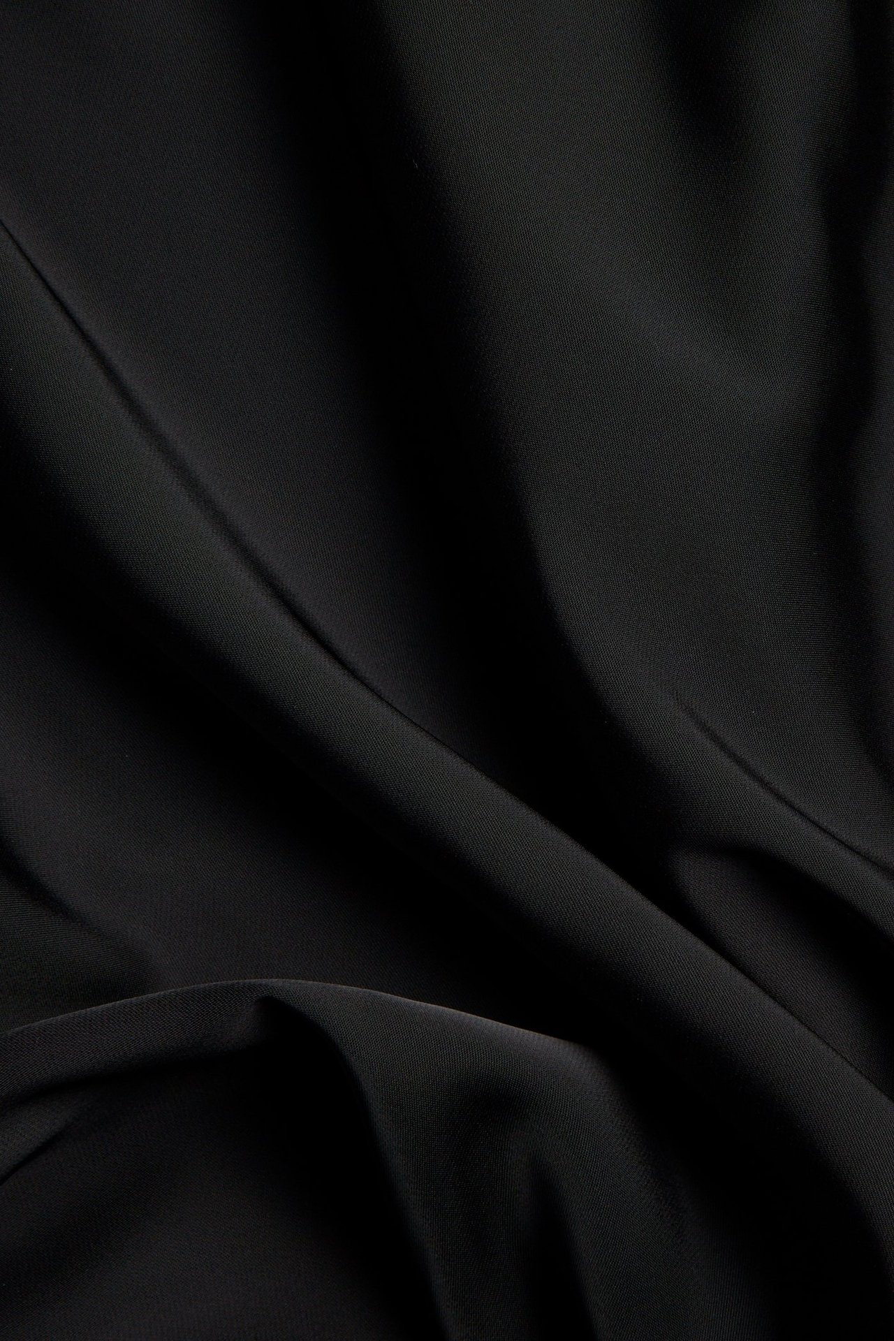 Mustan polyesterisatiinihameen kangas lähikuvassa, jossa on pehmeitä laskoksia.