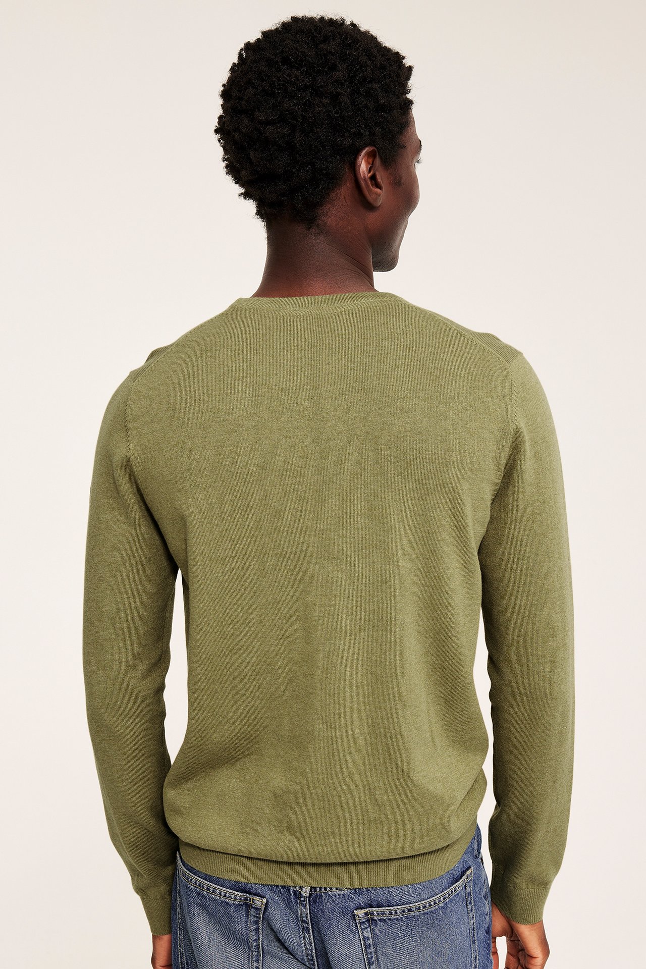Mann sett bakfra, iført en grønn crewneck-genser og blå jeans.