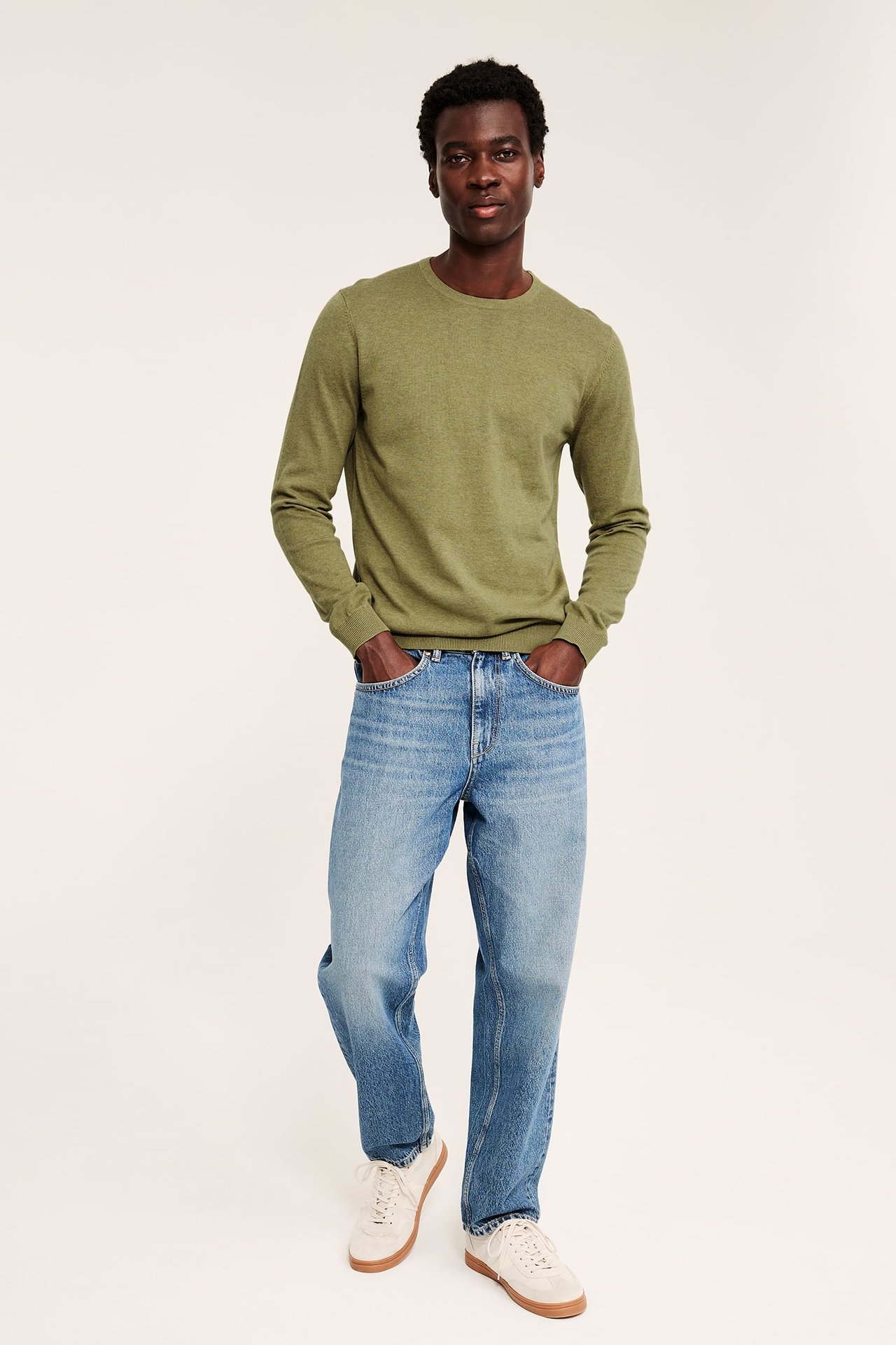 Frontbilde av mann i grønn langermet genser med rund hals, blå jeans og hvite joggesko.