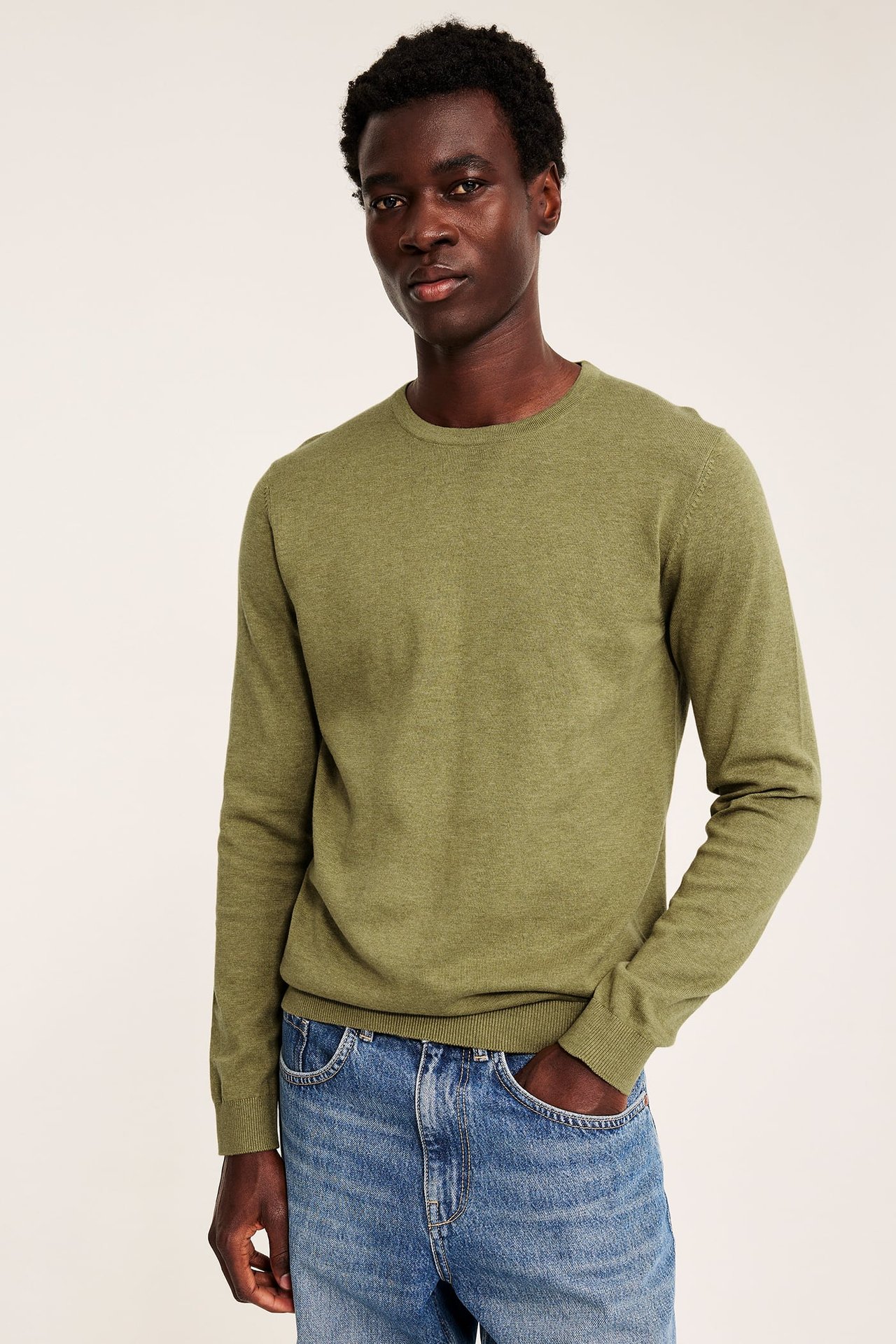 Frontbilde av mannlig modell i grønn genser med rund hals og blå jeans.