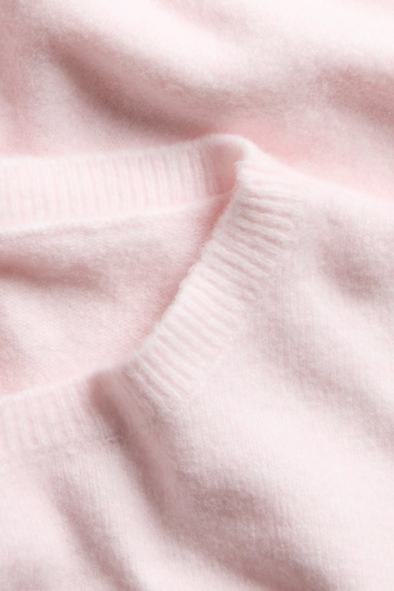 Nærbilde av en lys rosa finstrikket topp med båthals og myk tekstur.