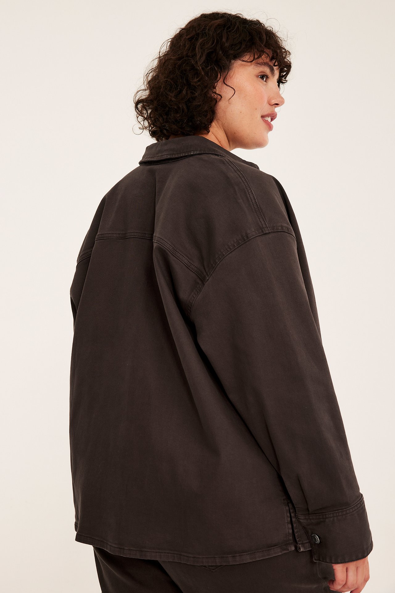 Naisen sivukuva, yllään oversized tummanharmaa utility-takki ja tummat housut.